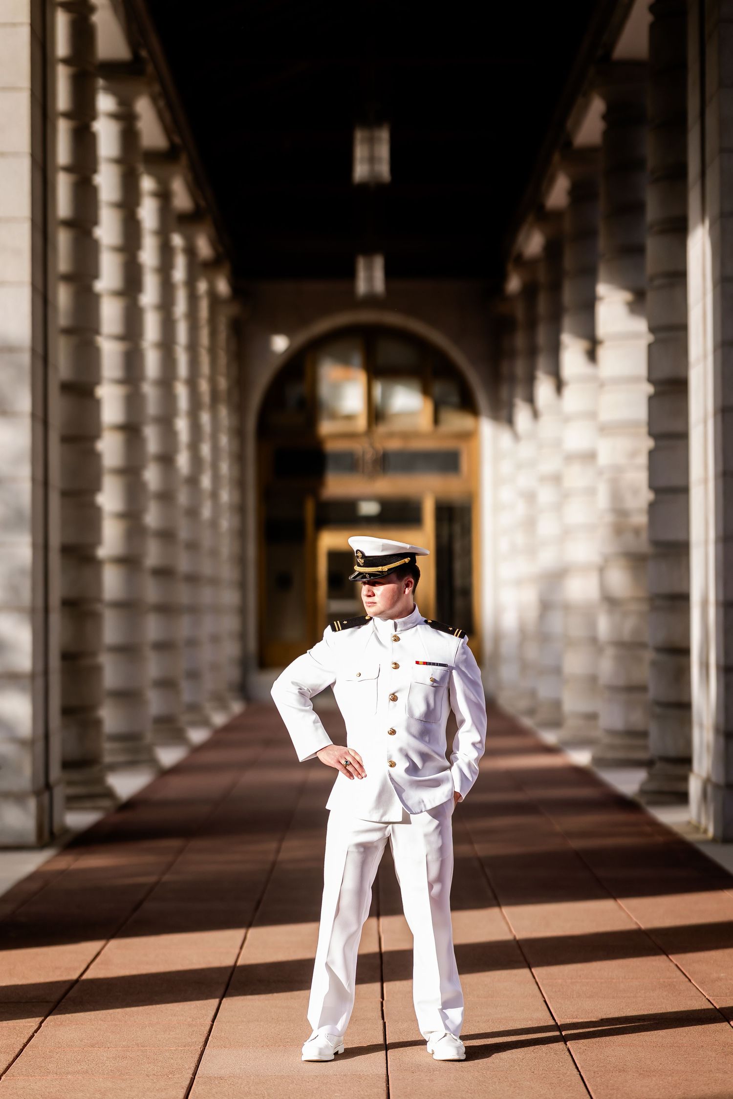 Naval officer in crisp white uniform standing in grand colonnade with dramatic lighting and shadows.