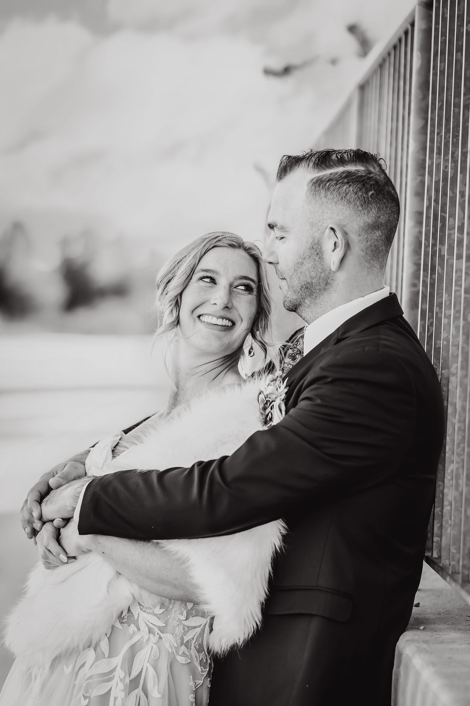A romantic black and white portrait of a couple embracing near a railing.