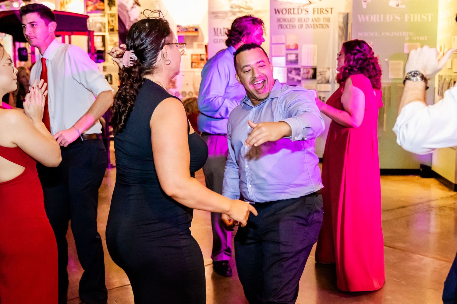 Wedding guests dance and celebrate on illuminated dance floor with purple lighting.