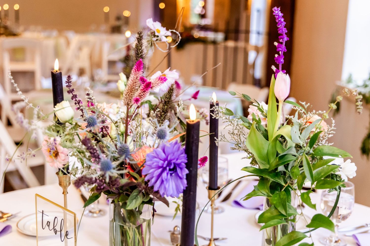 Elegant wedding table setting with wildflowers and purple candles in glass vases.