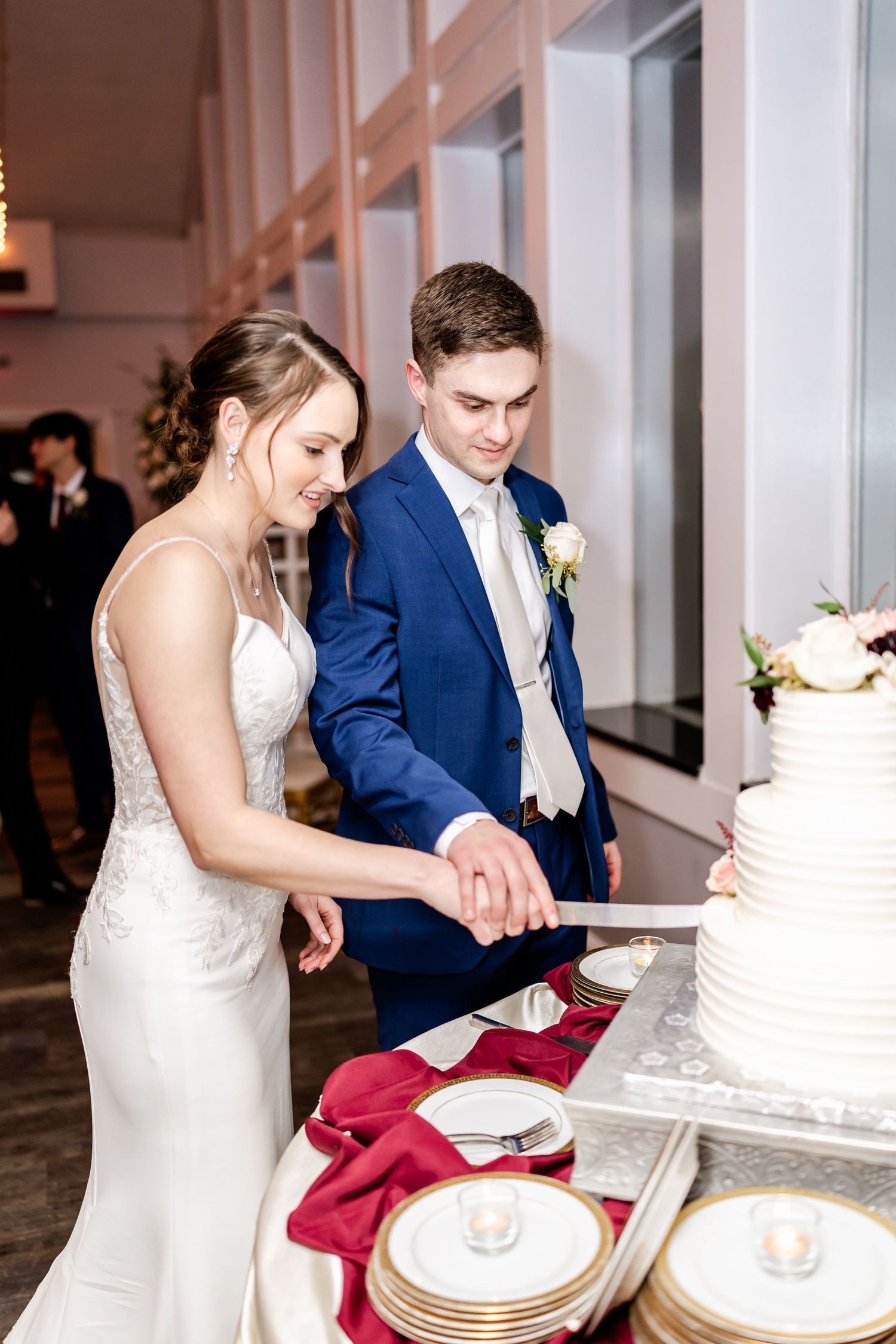 Newlyweds cut their elegant white wedding cake together at their reception.