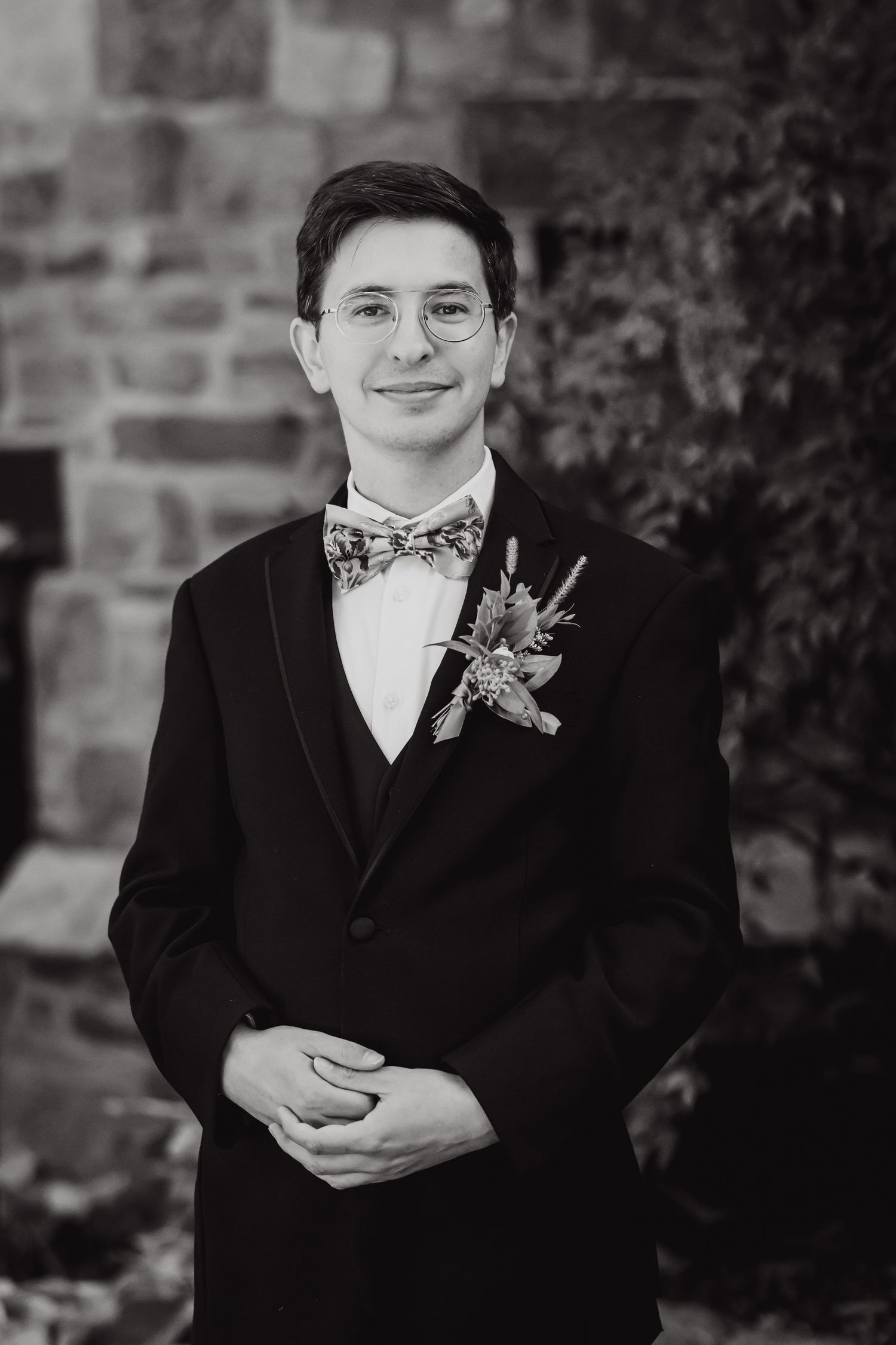 A formal portrait of a groom in a black tuxedo and floral bowtie with boutonniere.