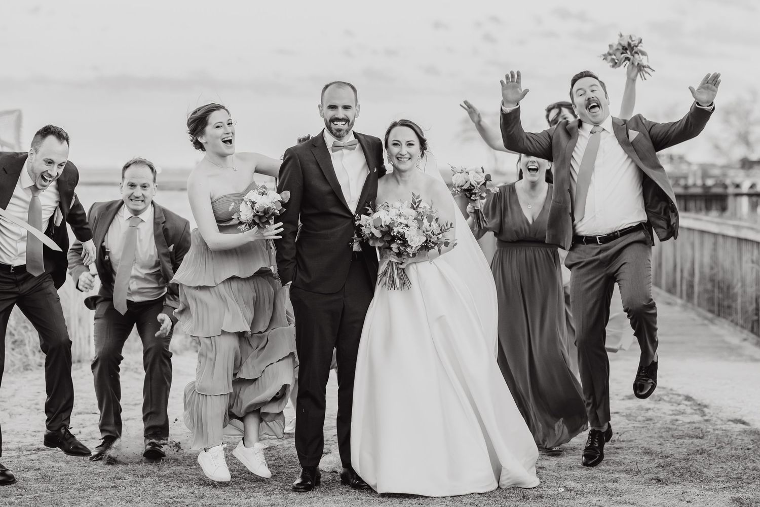 A joyful wedding party celebrating and jumping together outdoors in black and white photography.