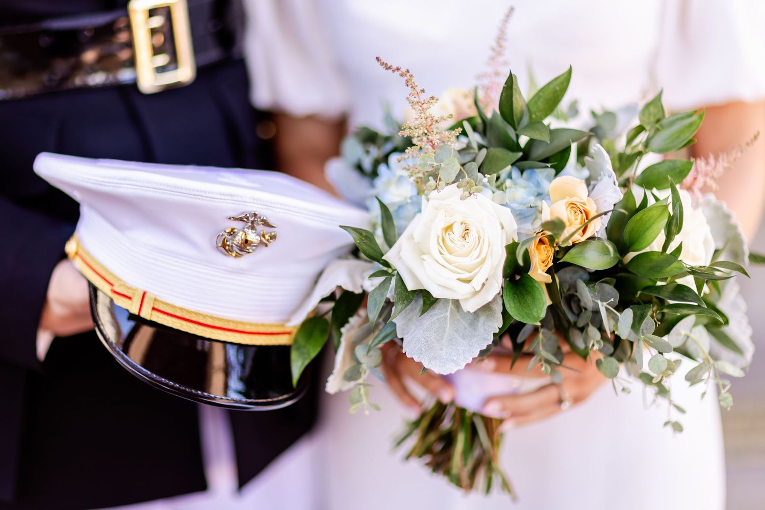 Marine service cap beside a white and green wedding bouquet featuring roses and mixed foliage.