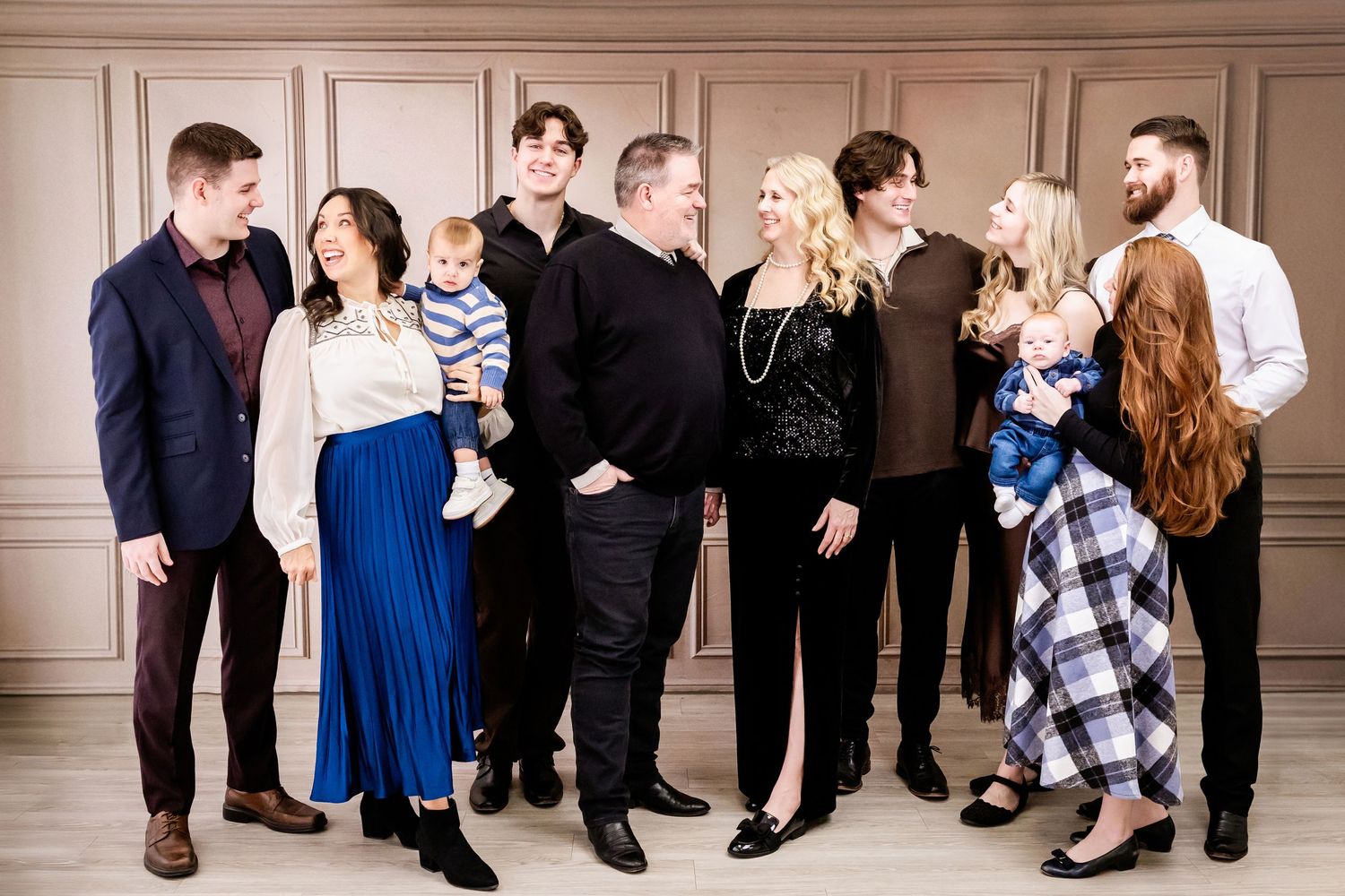 Extended family members arranged casually on white furniture for studio portrait.
