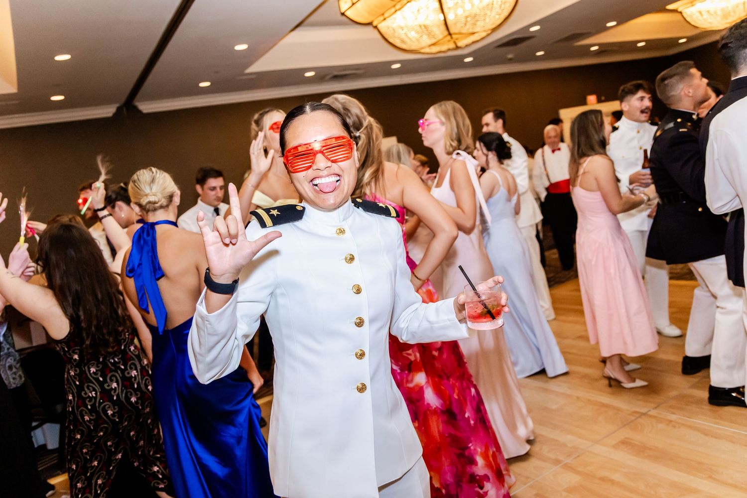 Wedding guests dancing in formal attire under elegant chandeliers at reception venue.
