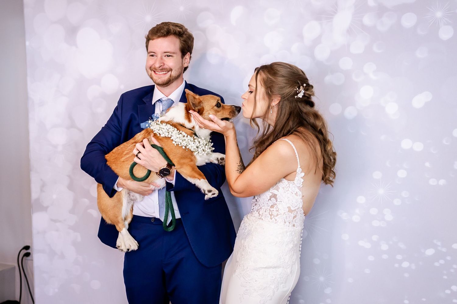 A joyful wedding couple shares a moment with their small dog during formal portraits.