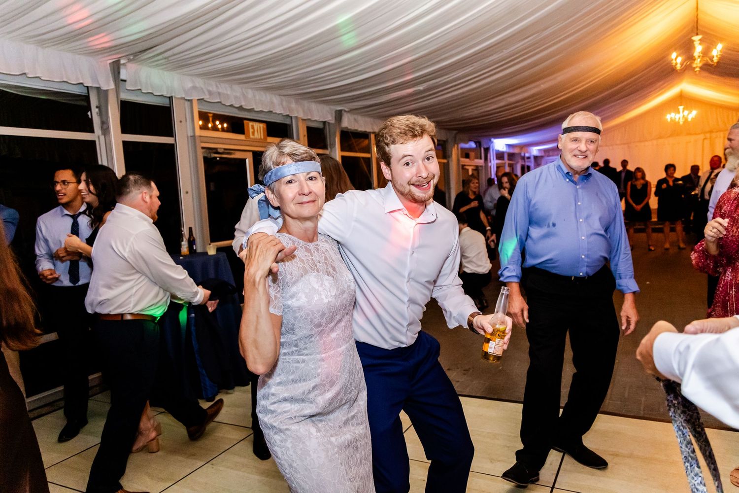 Wedding reception guests dancing and celebrating in an elegant tent venue with chandelier lighting.