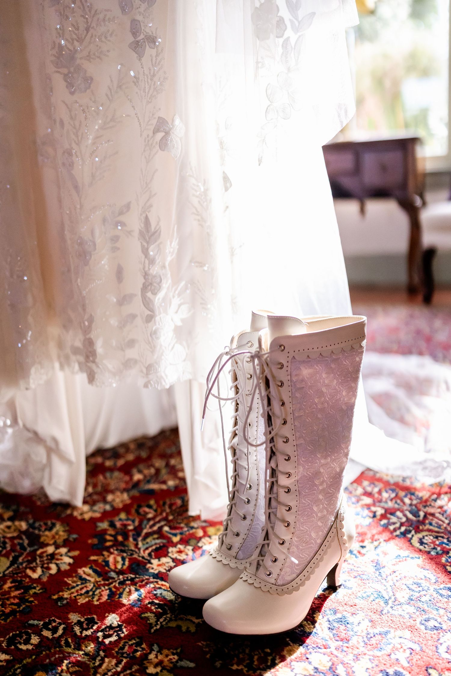 Vintage white Victorian-style lace-up boots displayed on an ornate patterned carpet.