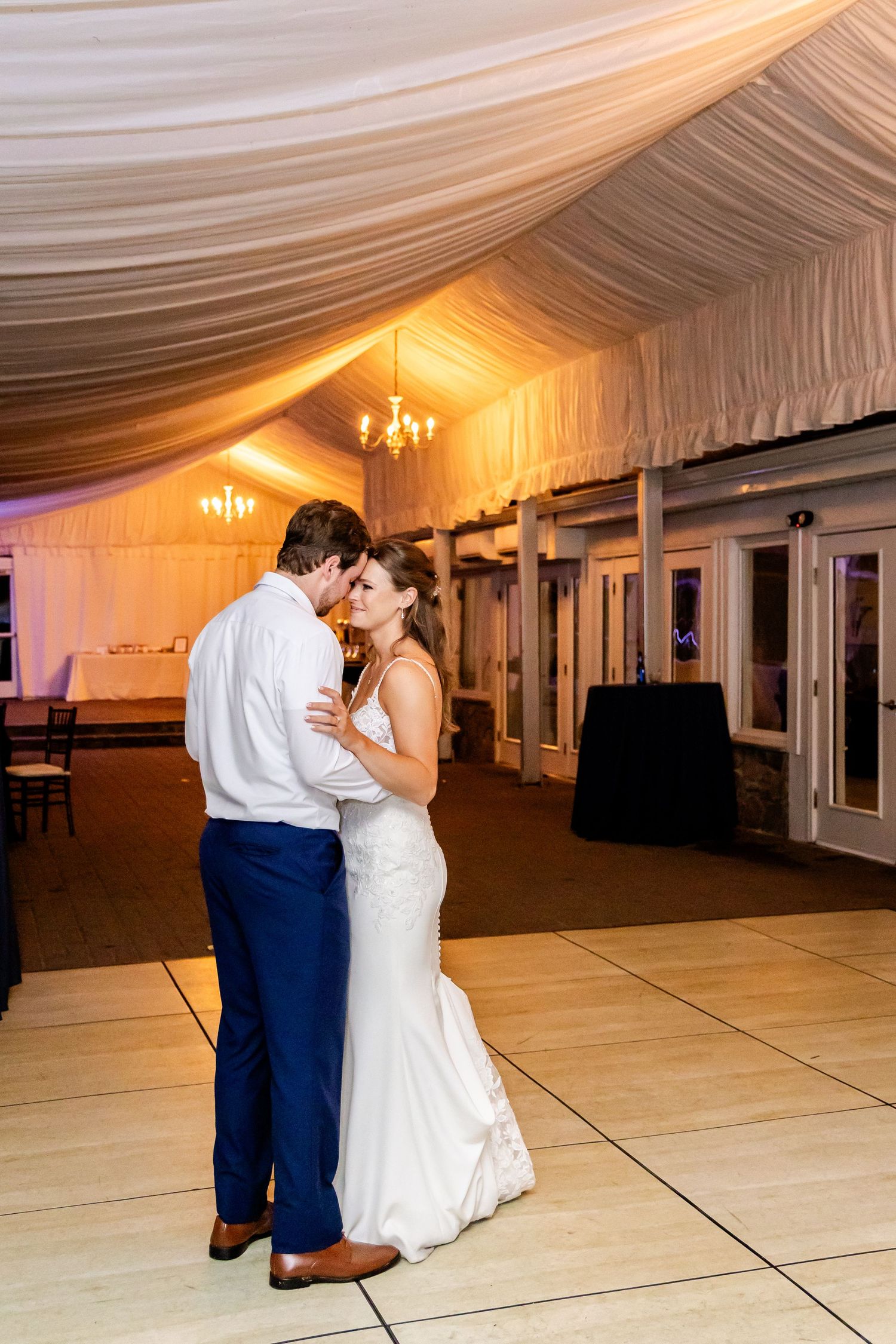 A couple shares an intimate slow dance under warm lighting in their reception venue.