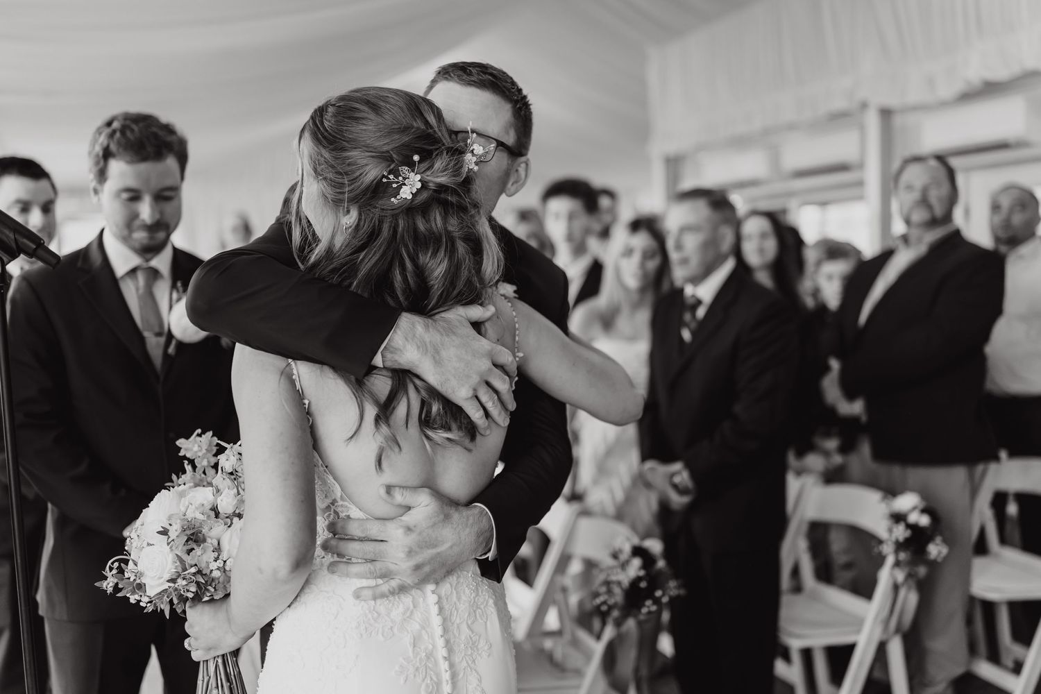 Wedding guests gather to witness an emotional embrace during an indoor ceremony.