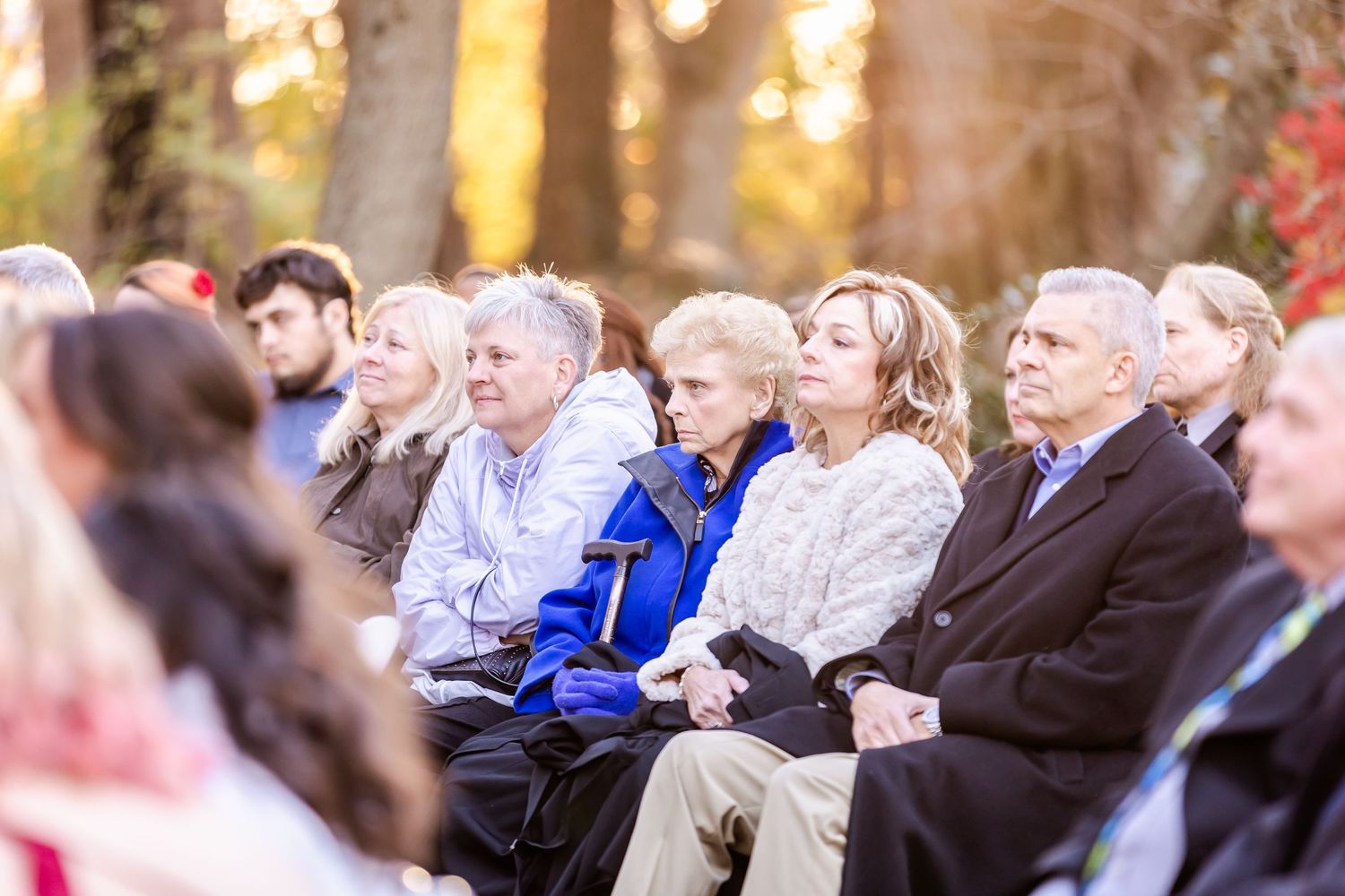 Wedding guests seated outdoors watching the ceremony in an autumn setting with golden sunlight.