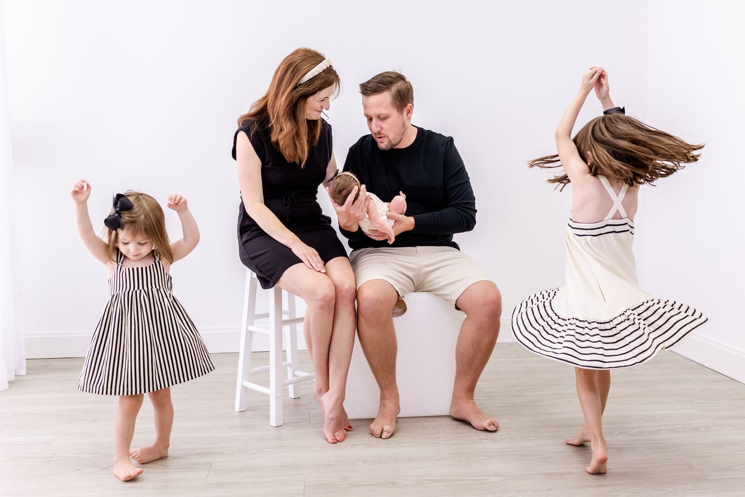 Family wearing white and neutral tones dance together in a bright studio setting for a lifestyle photoshoot.