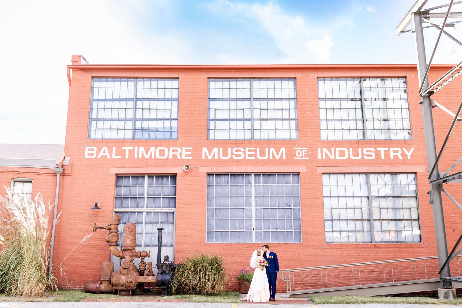 Exterior view of the red brick Baltimore Museum of Industry building with large windows and signage on a sunny day.