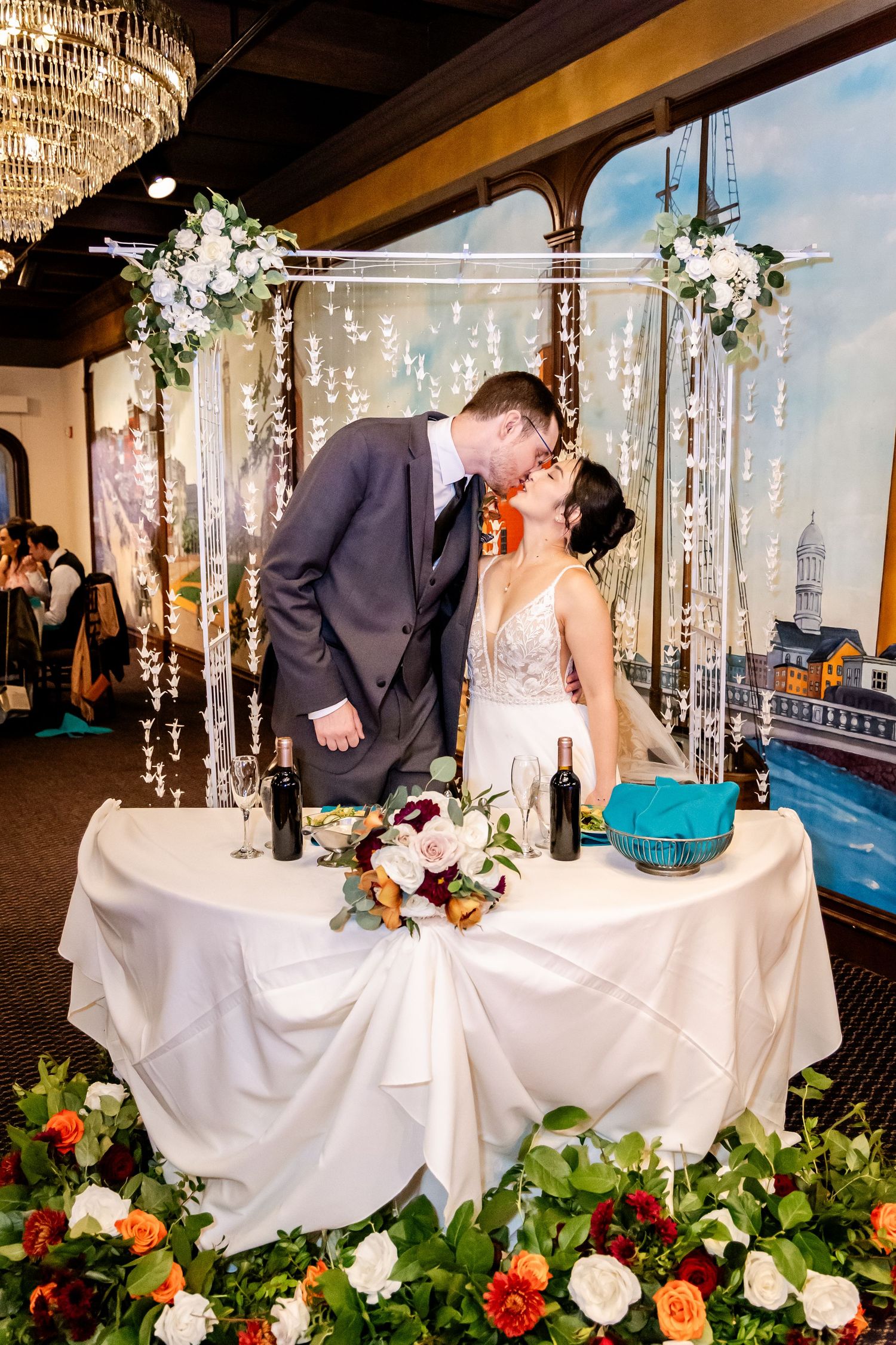 Wedding couple shares a romantic moment at their reception table decorated with floral arrangements and twinkling lights.