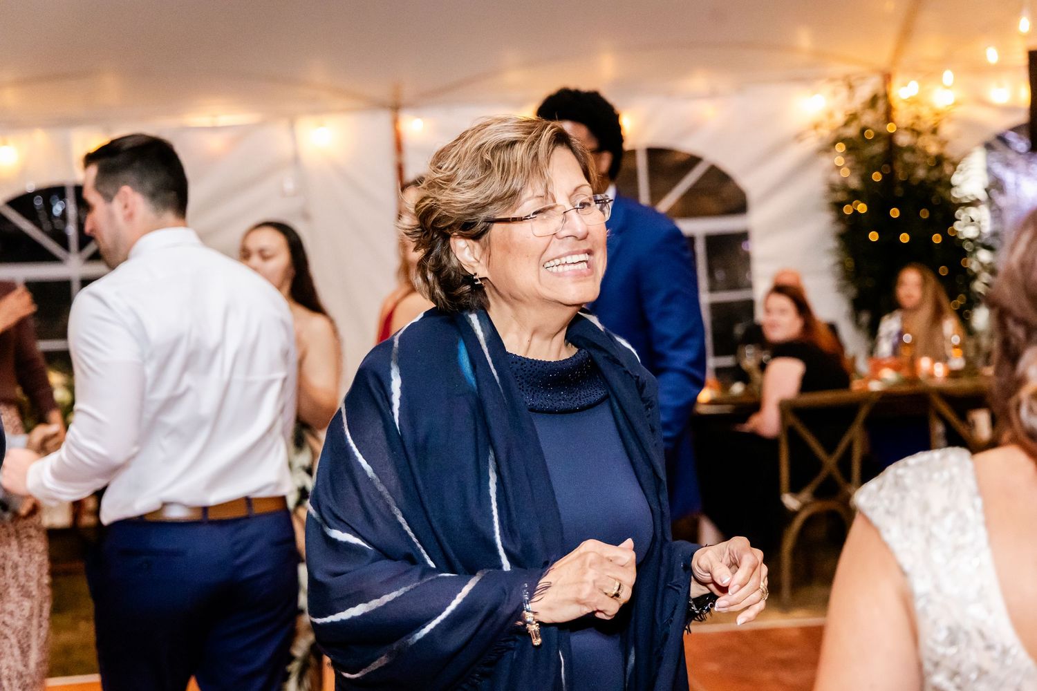 Wedding guests dancing and celebrating under a beautifully lit reception tent in the evening.