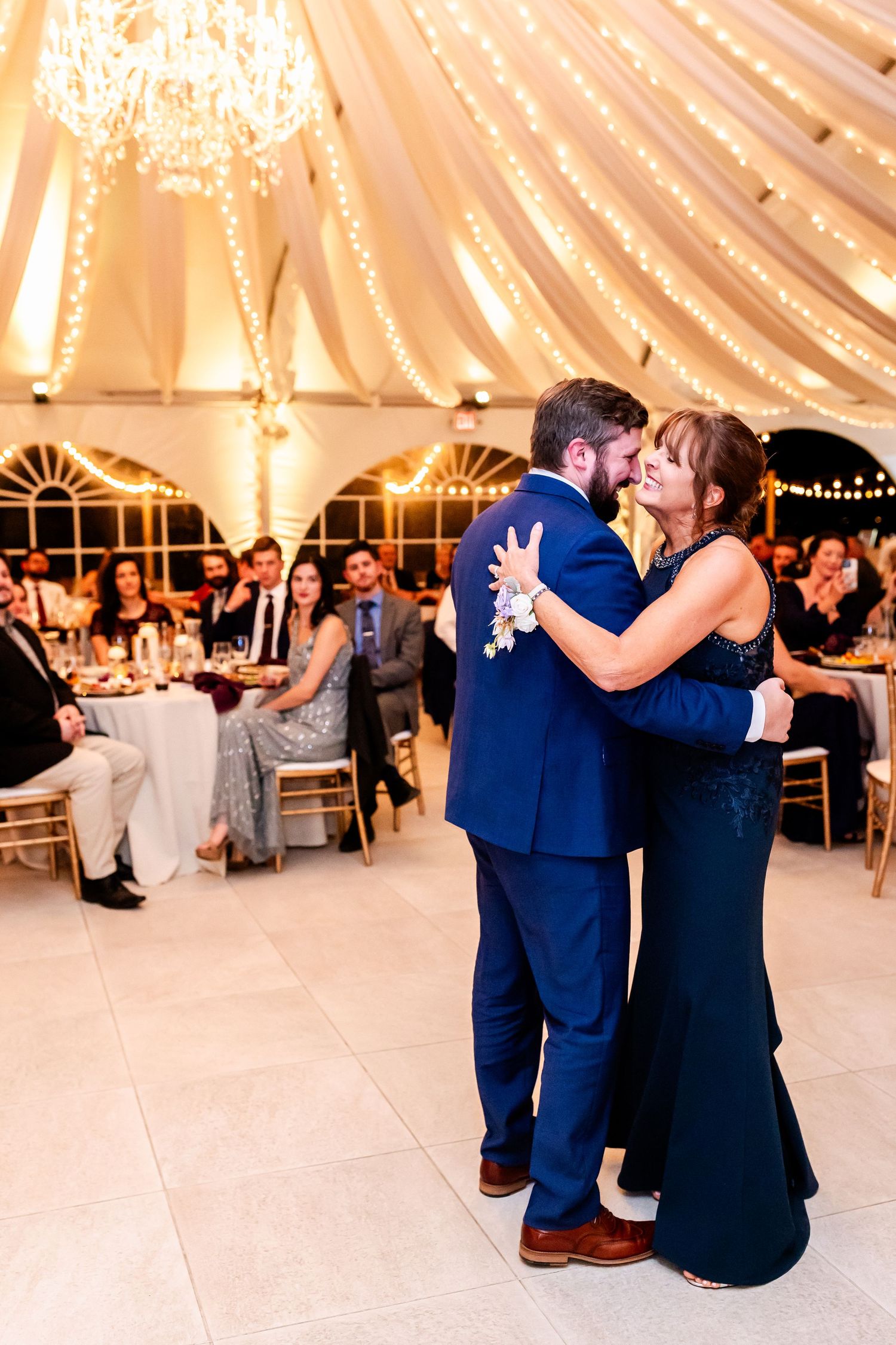 Wedding dance in tent venue with draped fabric ceiling and chandelier lighting.