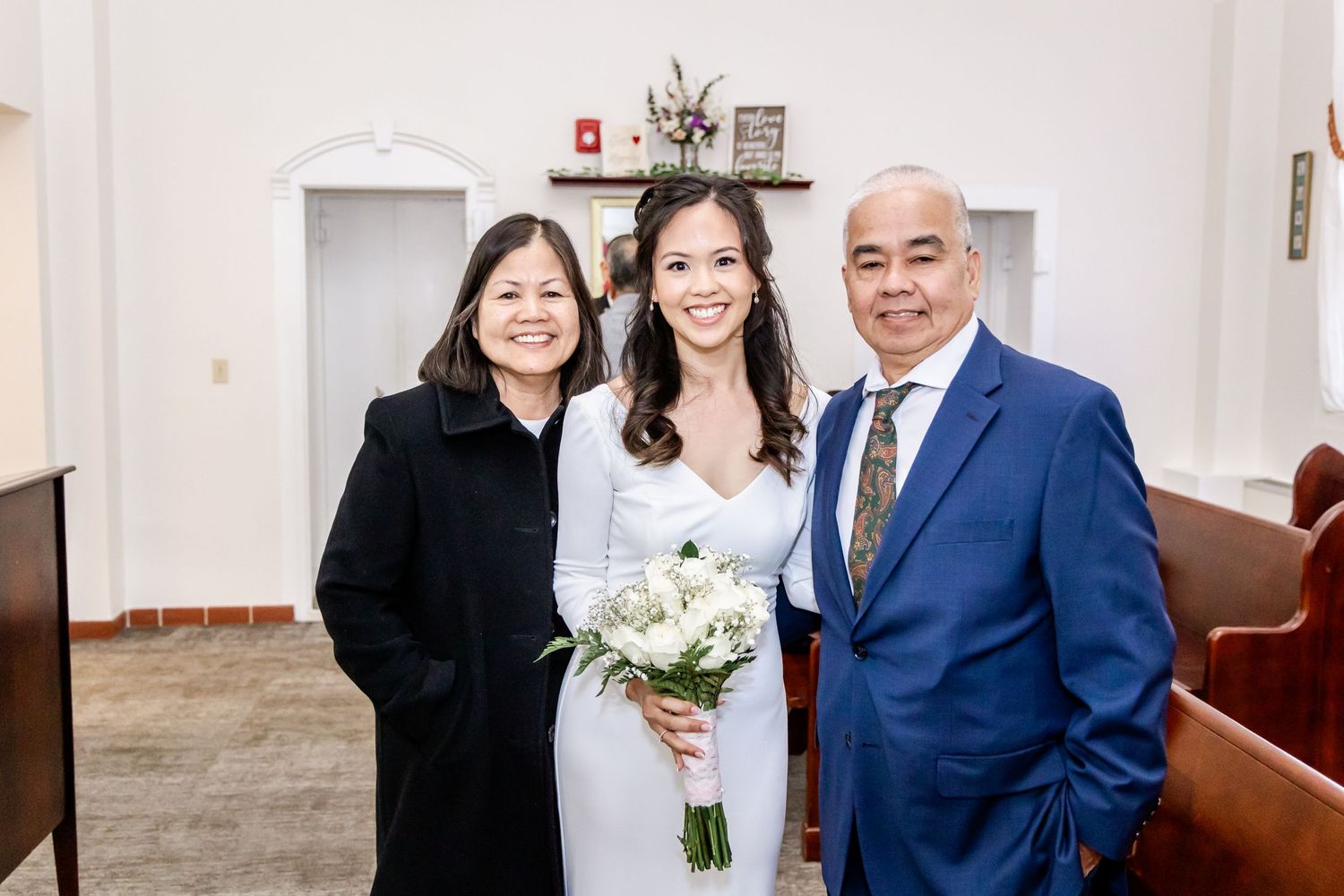 A joyful wedding gathering in an indoor venue with white walls and warm lighting.