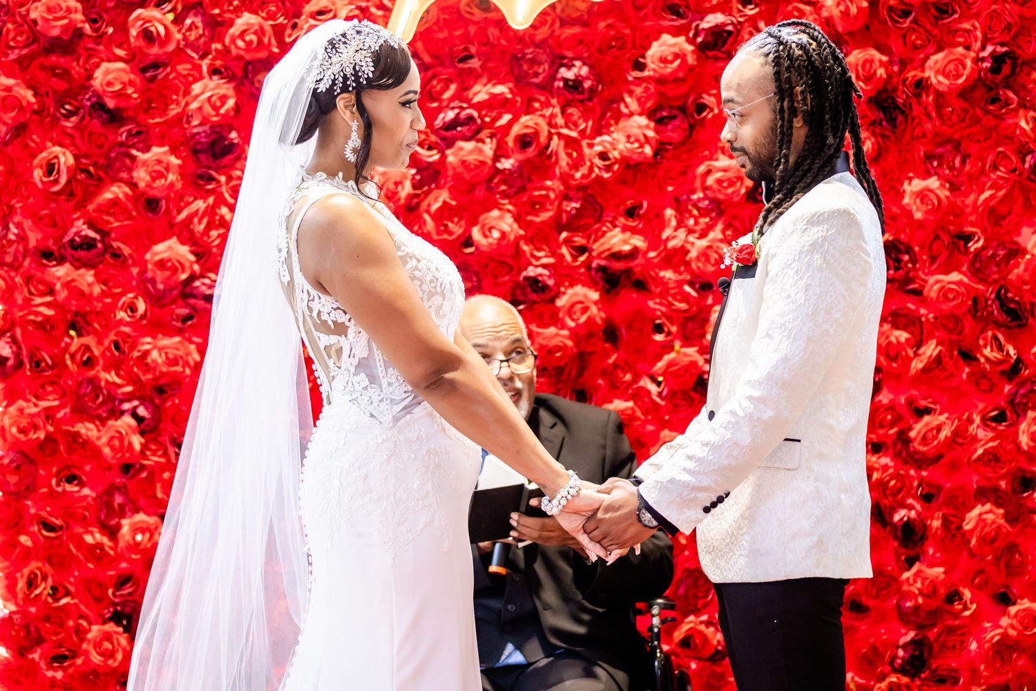 Wedding ceremony with dramatic red rose wall backdrop and white decor.