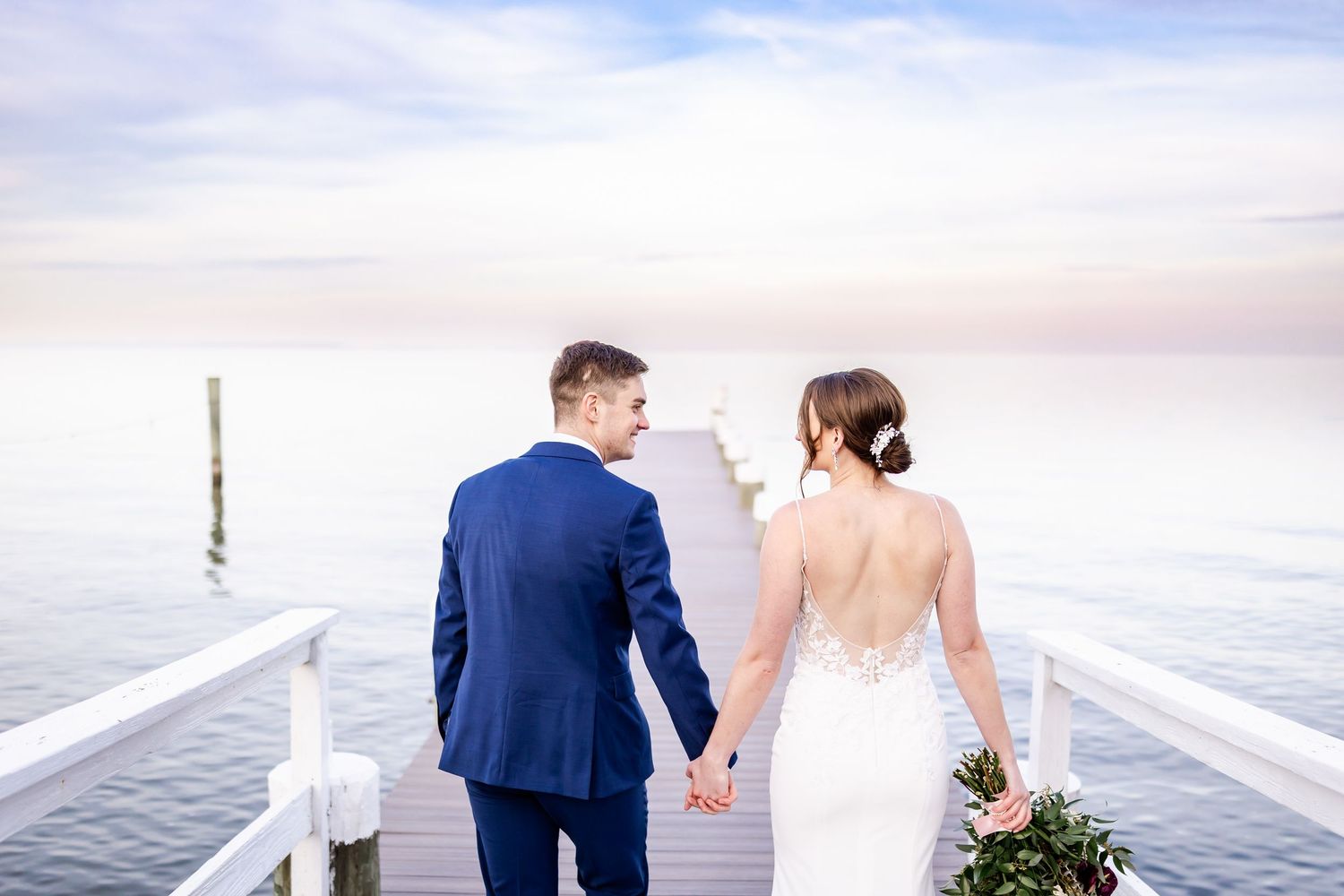Newlywed couple shares intimate moment on waterfront deck during golden hour.