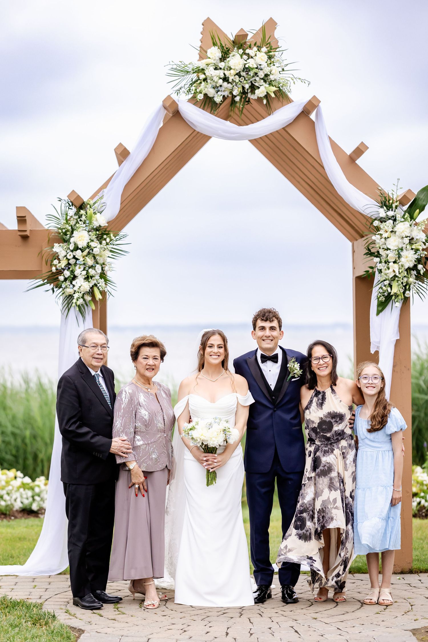 Outdoor wedding ceremony setup with wooden arch decorated with white floral arrangements.