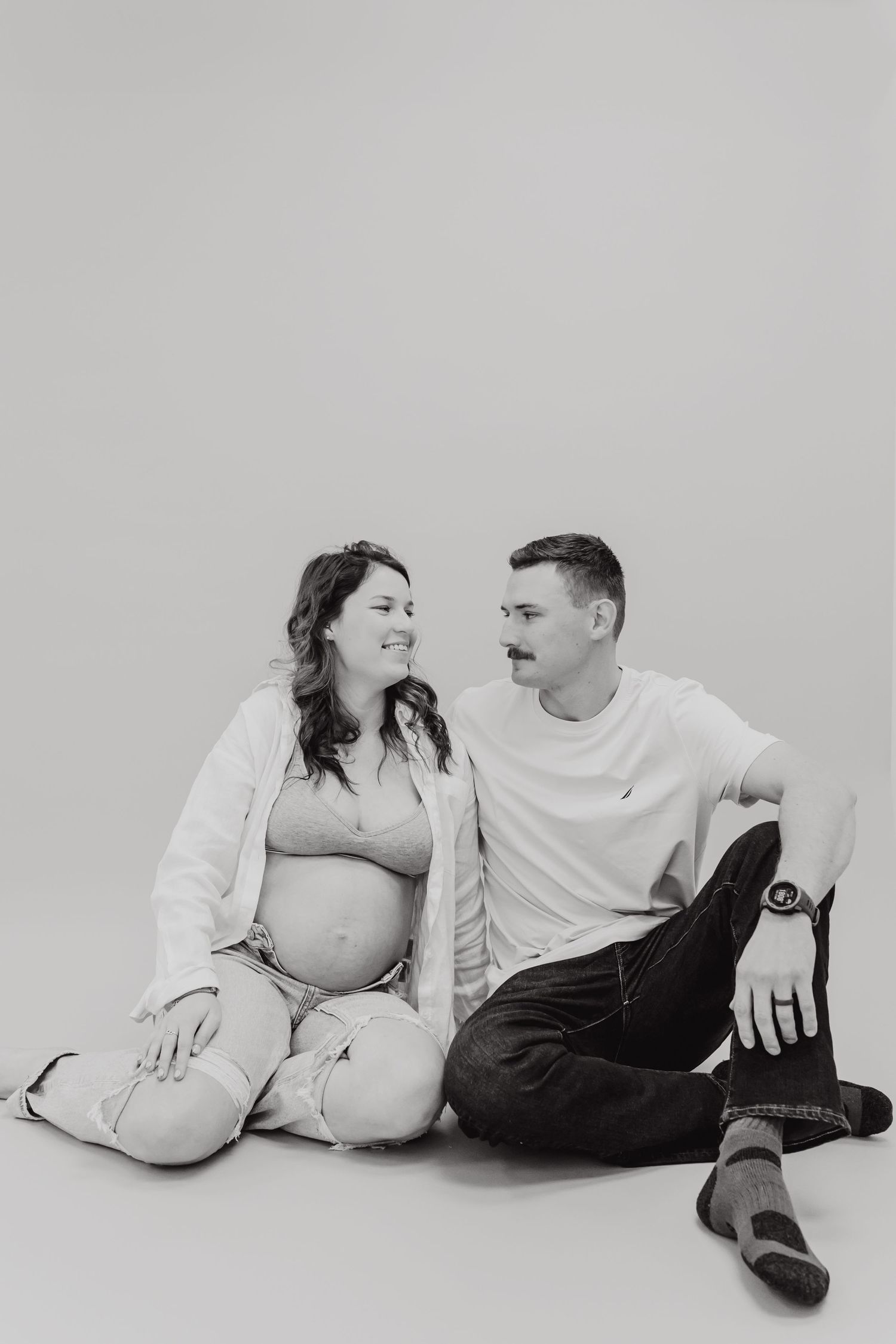 Black and white photo of a pregnant woman and man sitting together and smiling at each other.
