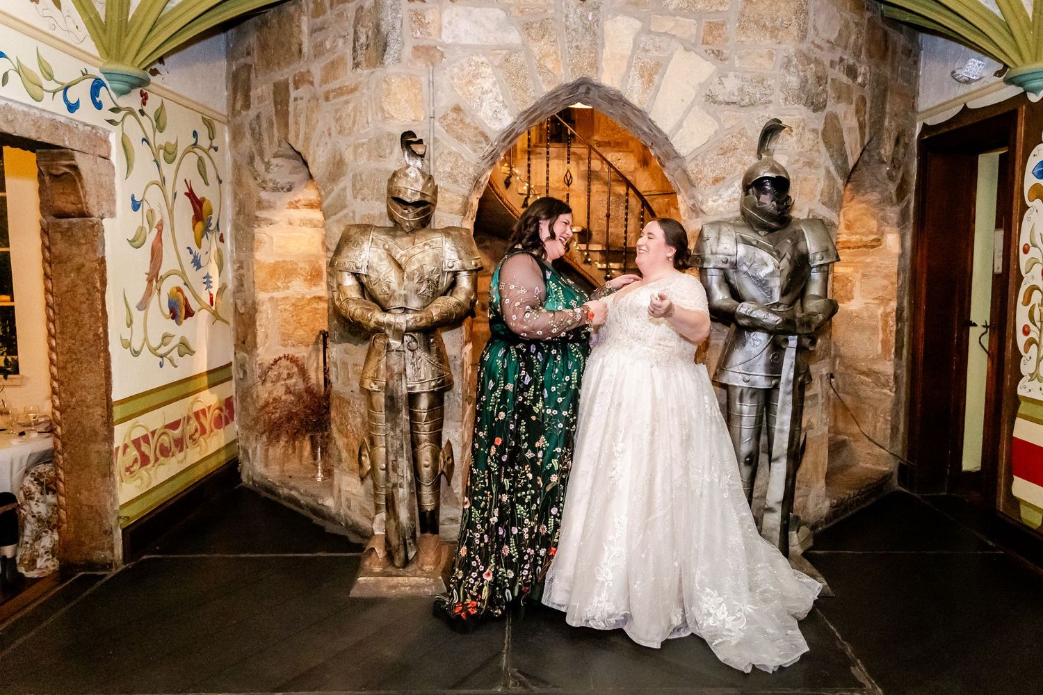 Wedding party posing between decorative knight statues in a castle-like stone archway.