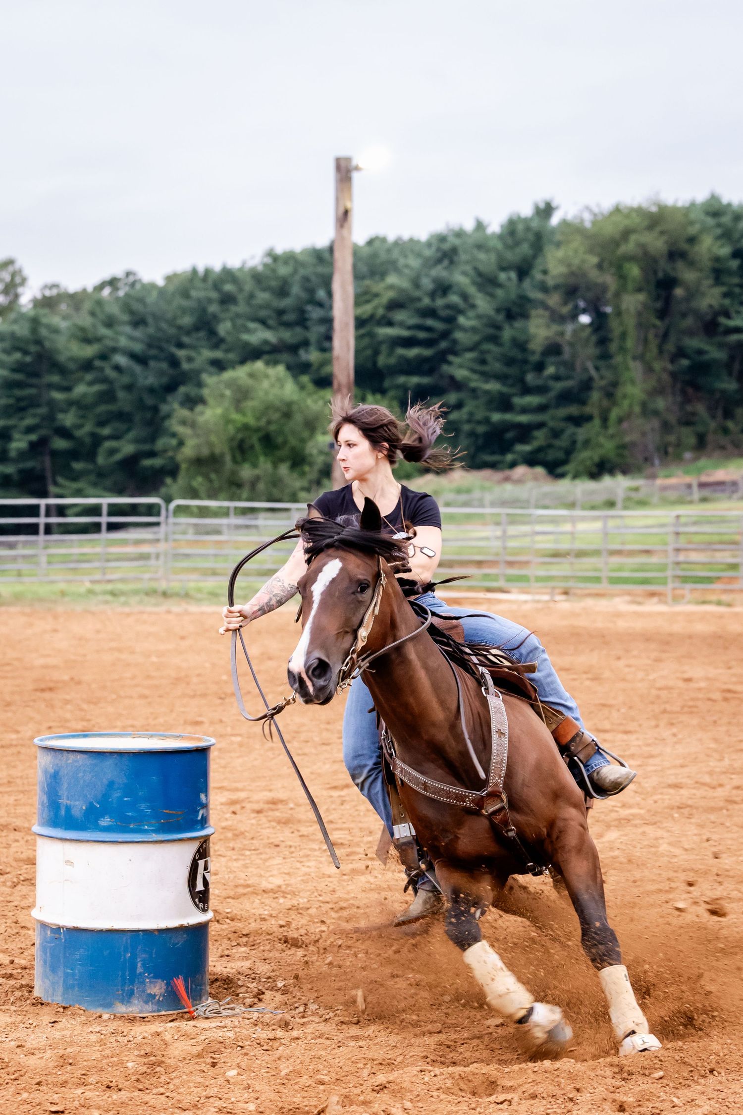 Barrel racer rounds a blue drum at high speed in a dirt arena.