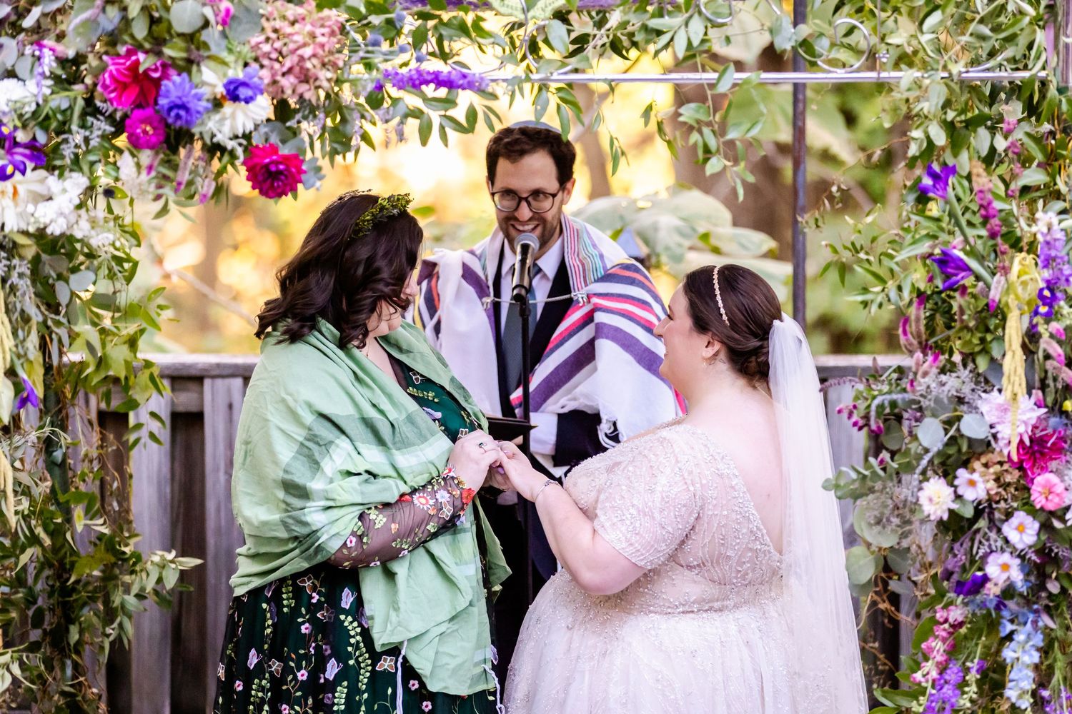 Wedding ceremony under a floral arch with couple and officiant exchanging vows.