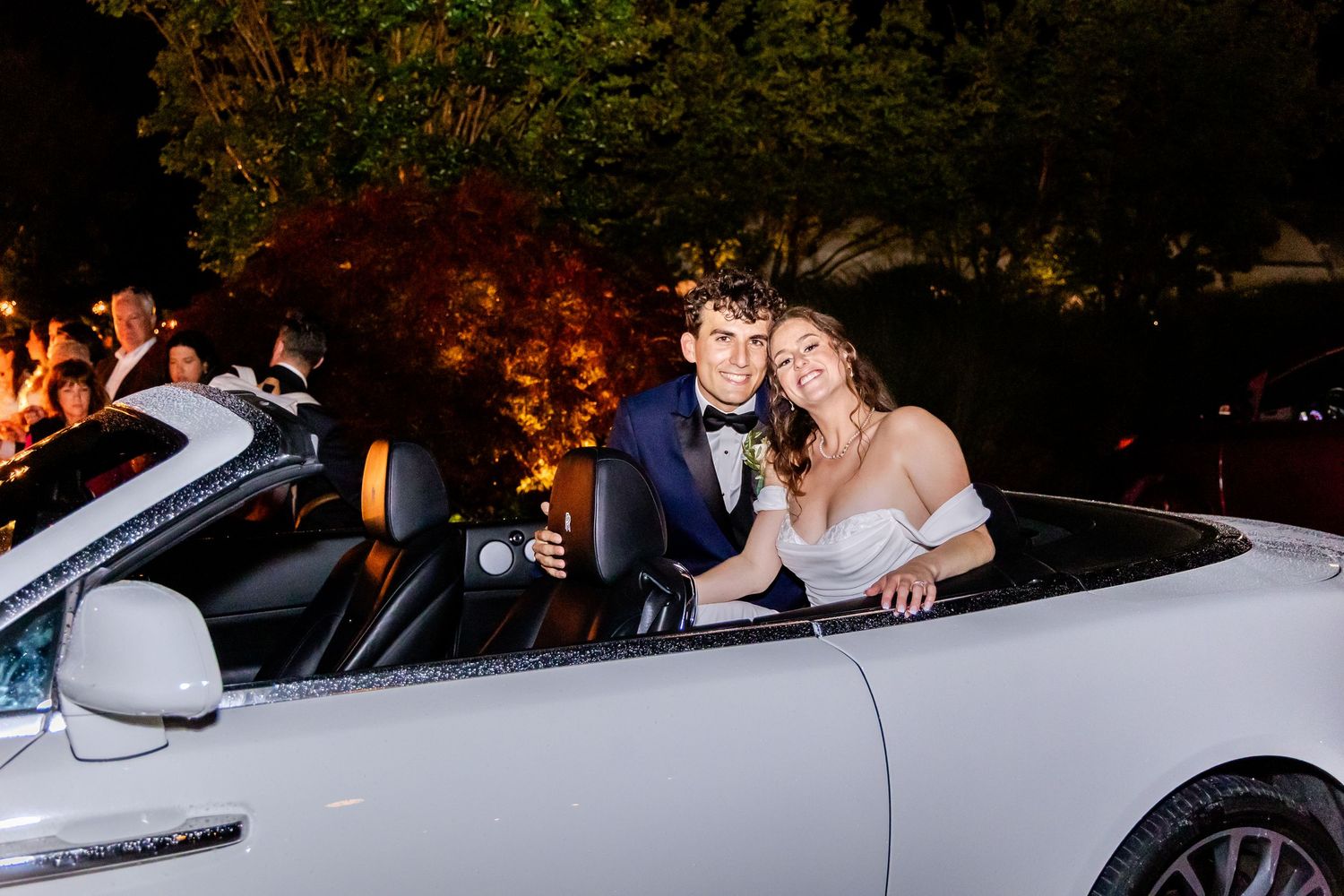 Newlyweds sit in a convertible car during their nighttime wedding exit.