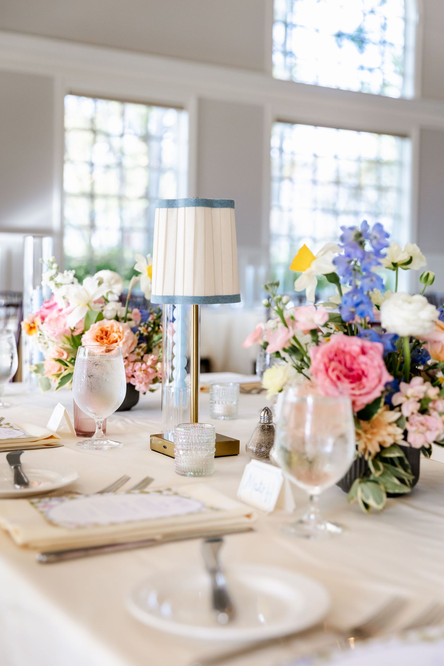 Elegant white wedding reception table setting with pastel floral centerpieces and crystal glassware.