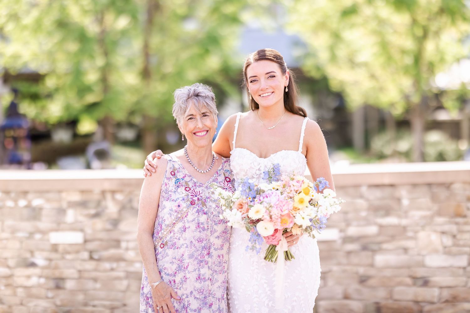 Garden wedding party gathering with stone wall backdrop and floral bouquets.