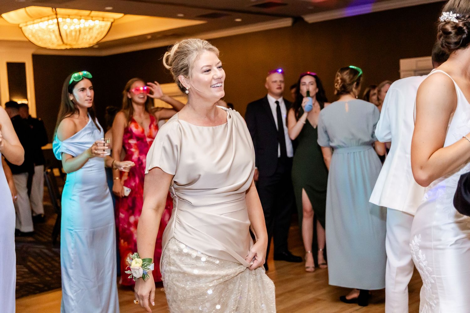Wedding reception guests dancing and celebrating in formal attire under ornate ballroom chandeliers.