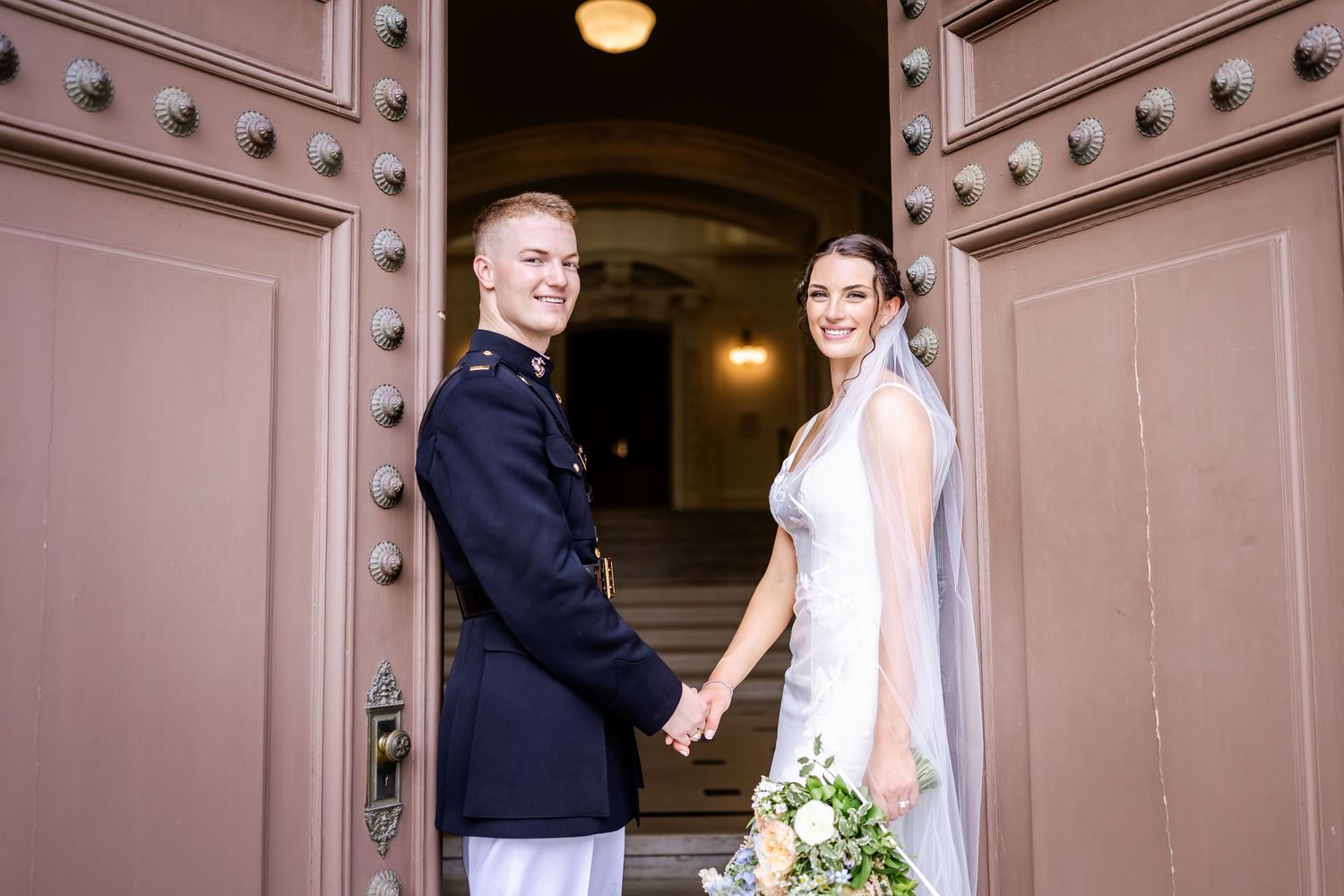 Wedding couple poses in doorway of historic building with ornate metal details.