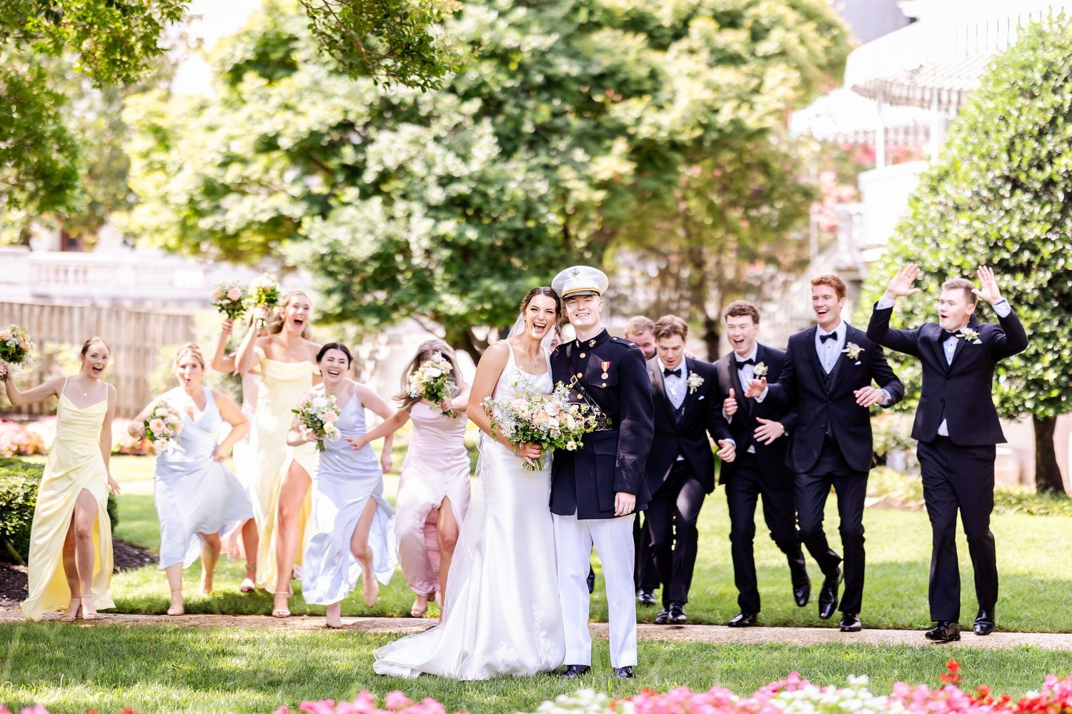Wedding party poses for formal photos on a sunny day in a garden setting.