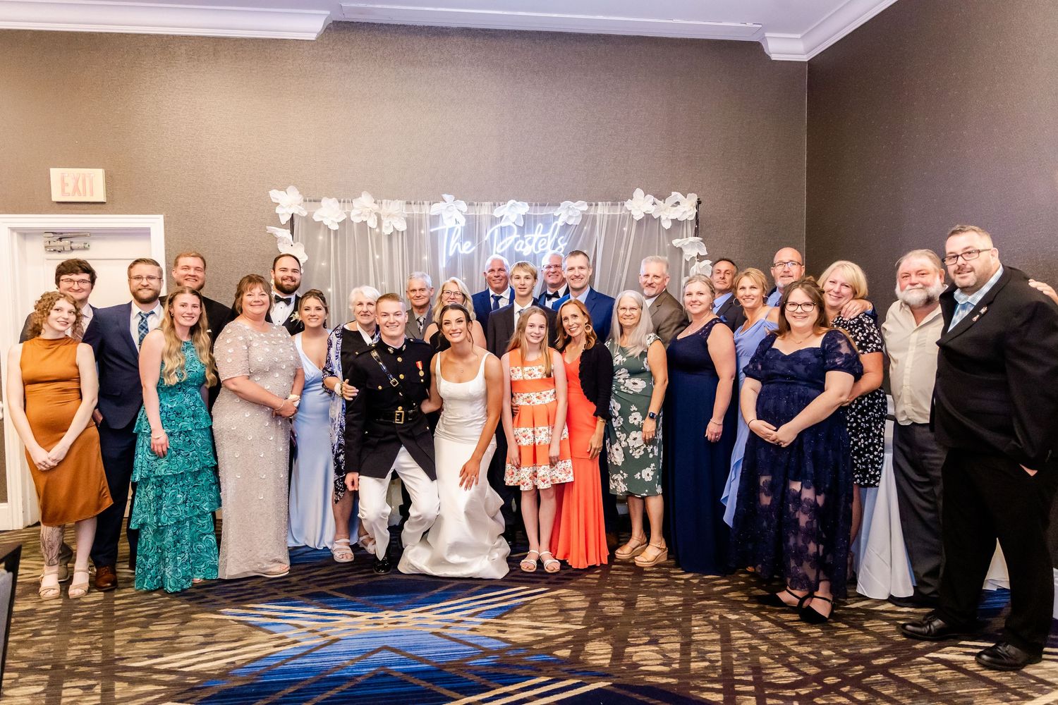 Large wedding party group photo with guests in formal attire gathered in an elegant indoor venue.