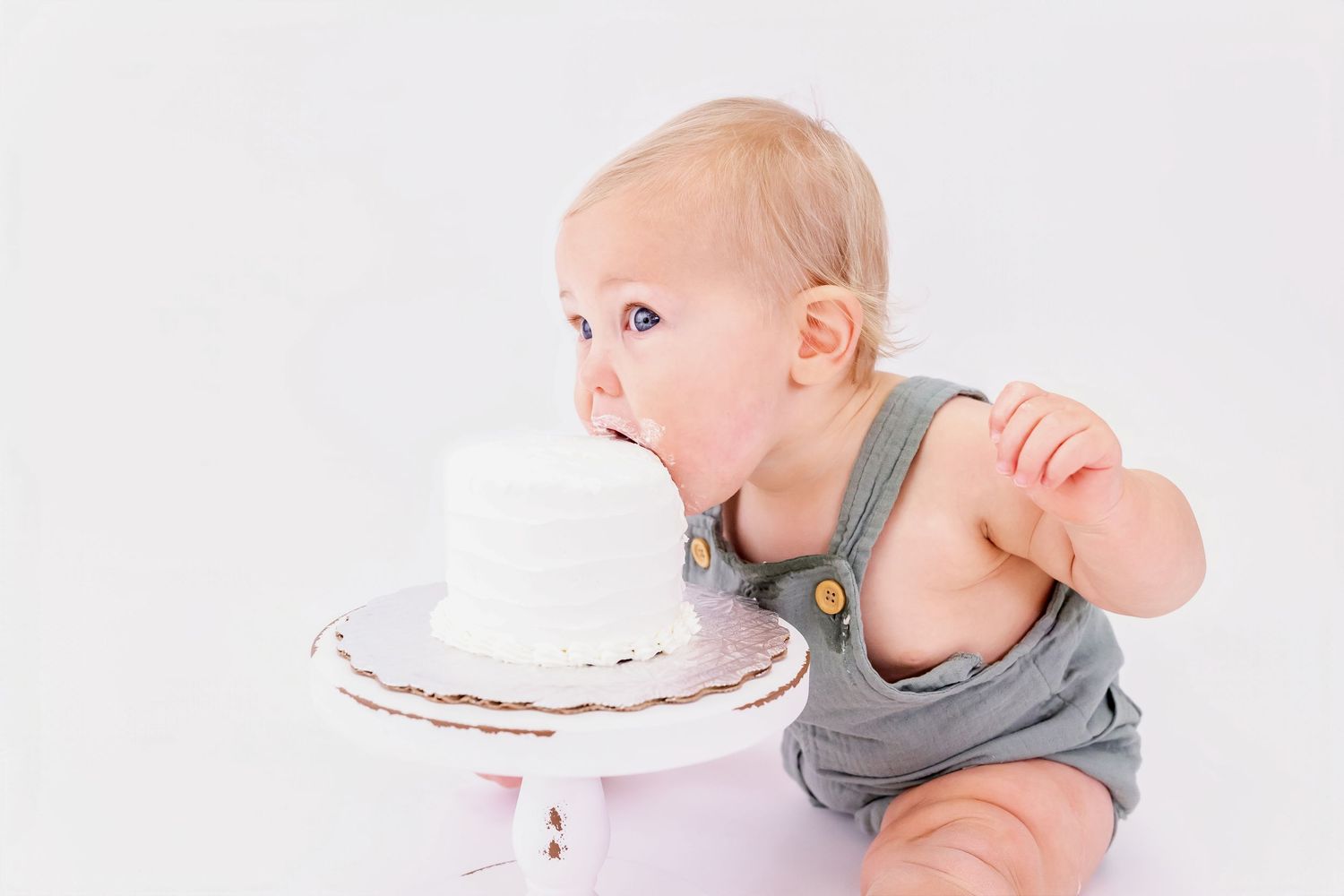 A baby in a gray onesie enjoys eating cake while sitting at a table in a series of progressive shots.