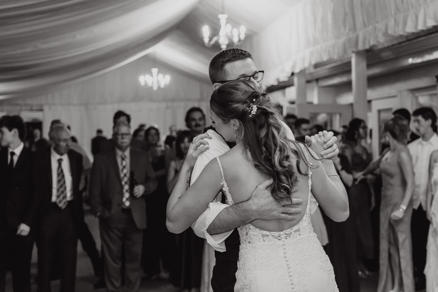 Black and white photo of couple sharing first dance at wedding reception under draped ceiling.