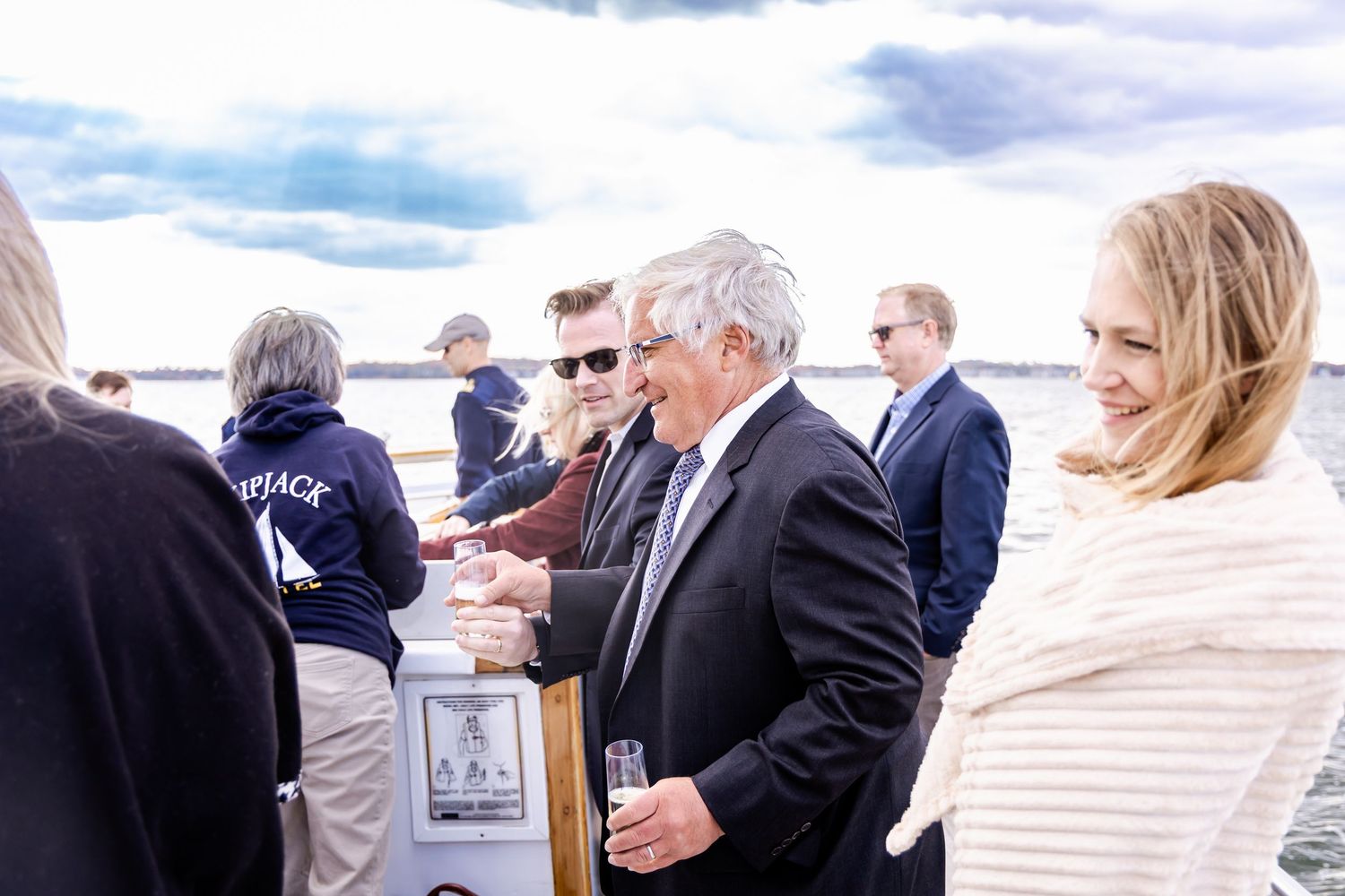 Group of professionals networking on a boat deck near the water on a cloudy day.