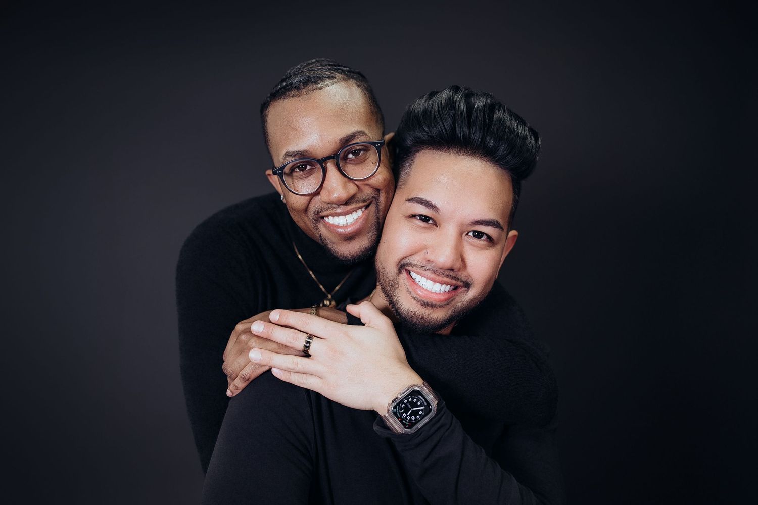 Friends sharing a warm embrace against dark background in studio setting.