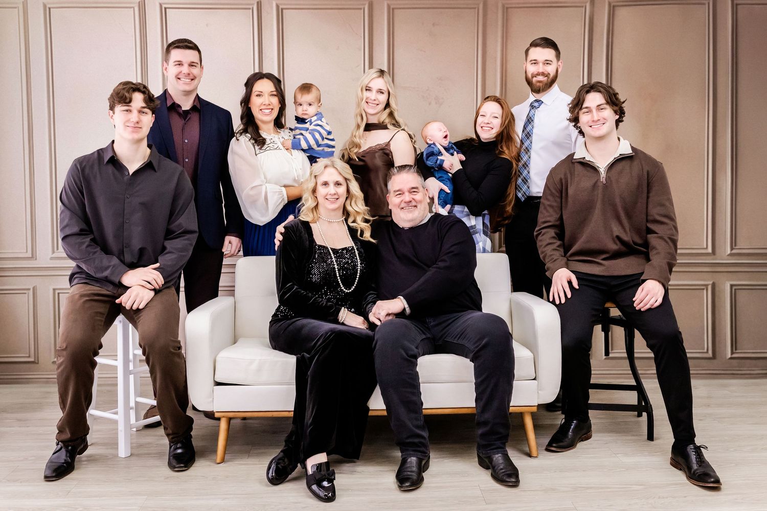 Large family group poses together on white furniture in formal studio setting.
