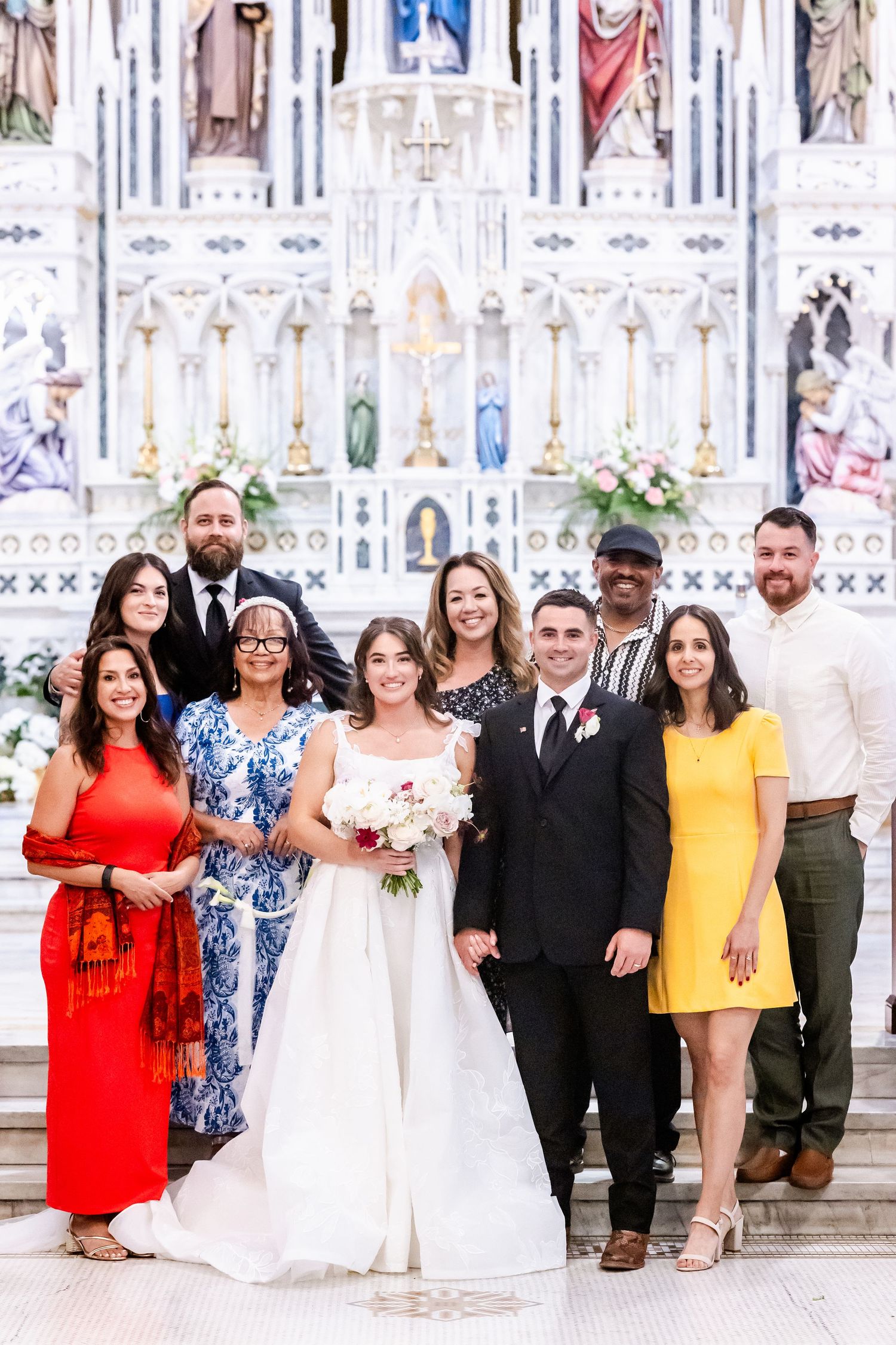 Wedding party members posing together in front of an ornate white church altar.