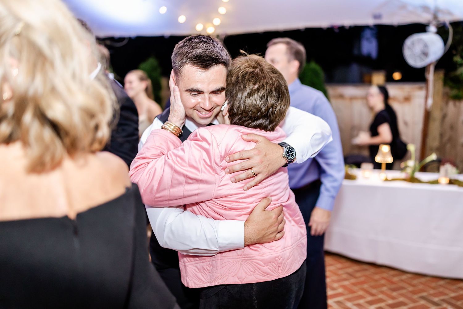 Two people share an intimate dance embrace at an indoor wedding reception with string lights overhead.