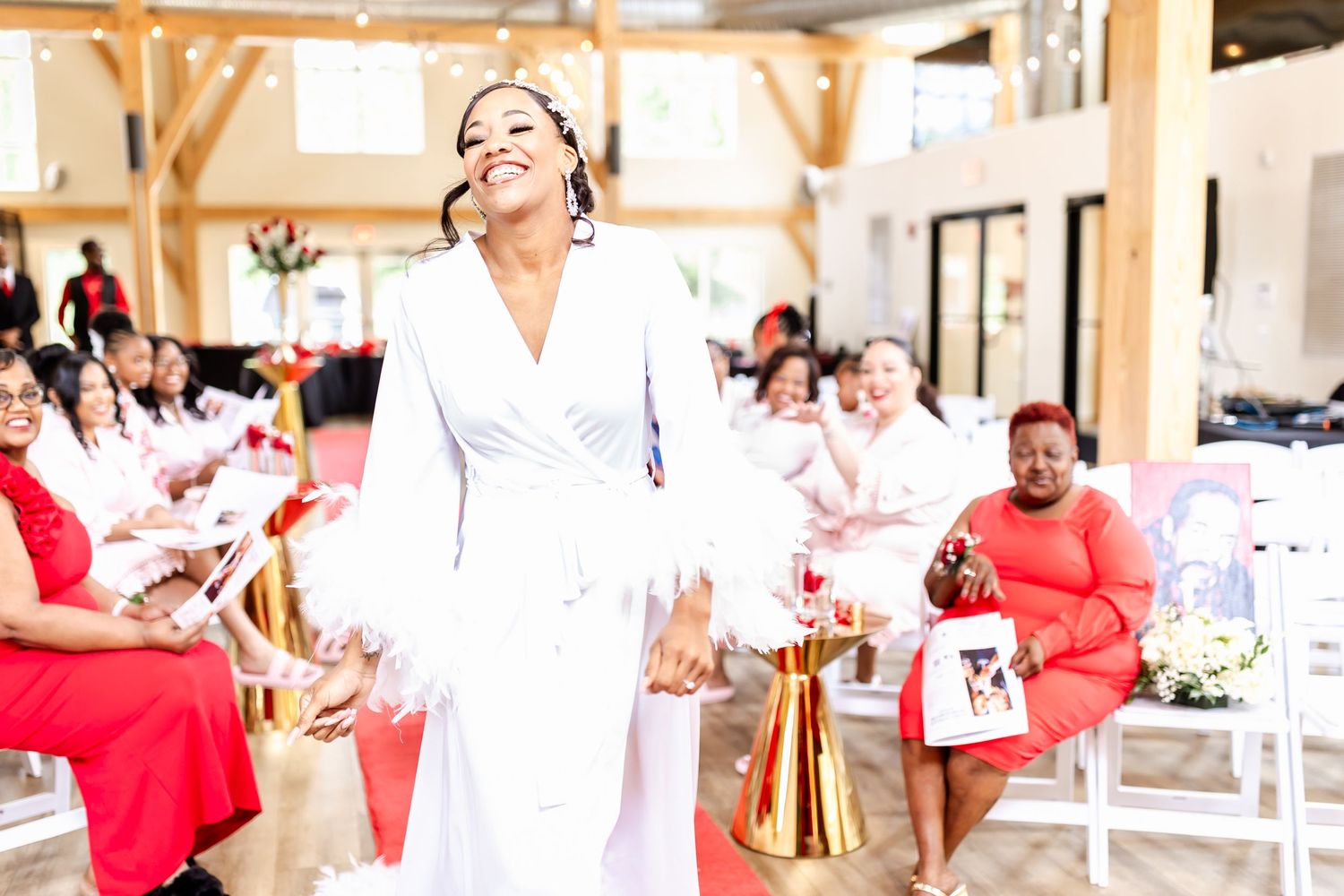 Elegant wedding venue interior with exposed beams and guests seated along a red-carpeted aisle.