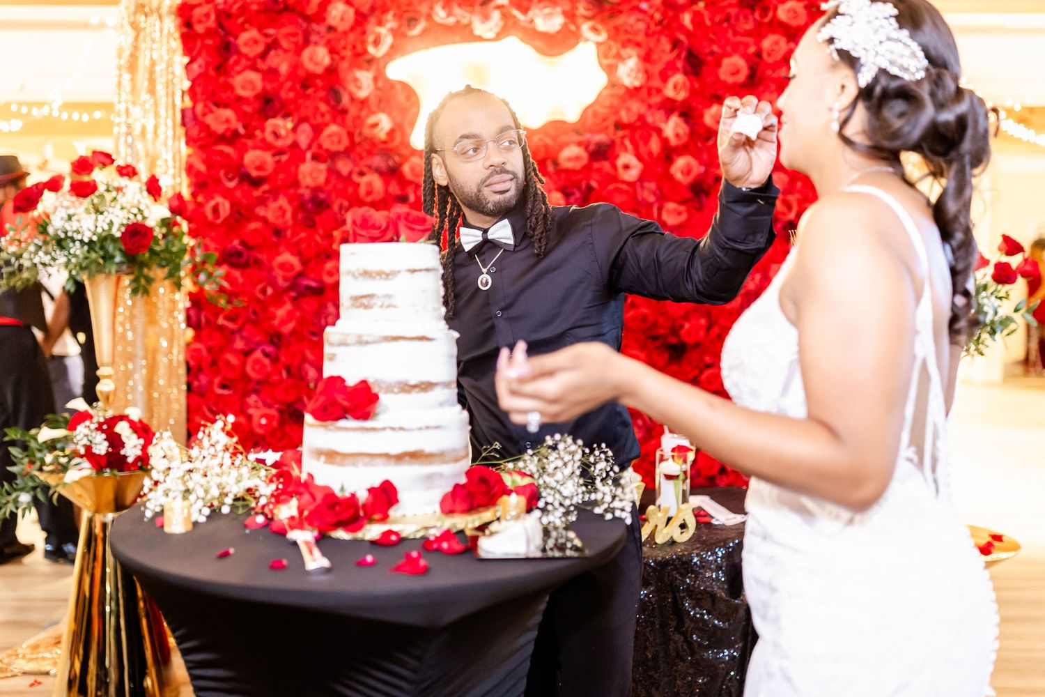 Celebratory moment at wedding reception with cake and red rose wall decoration.