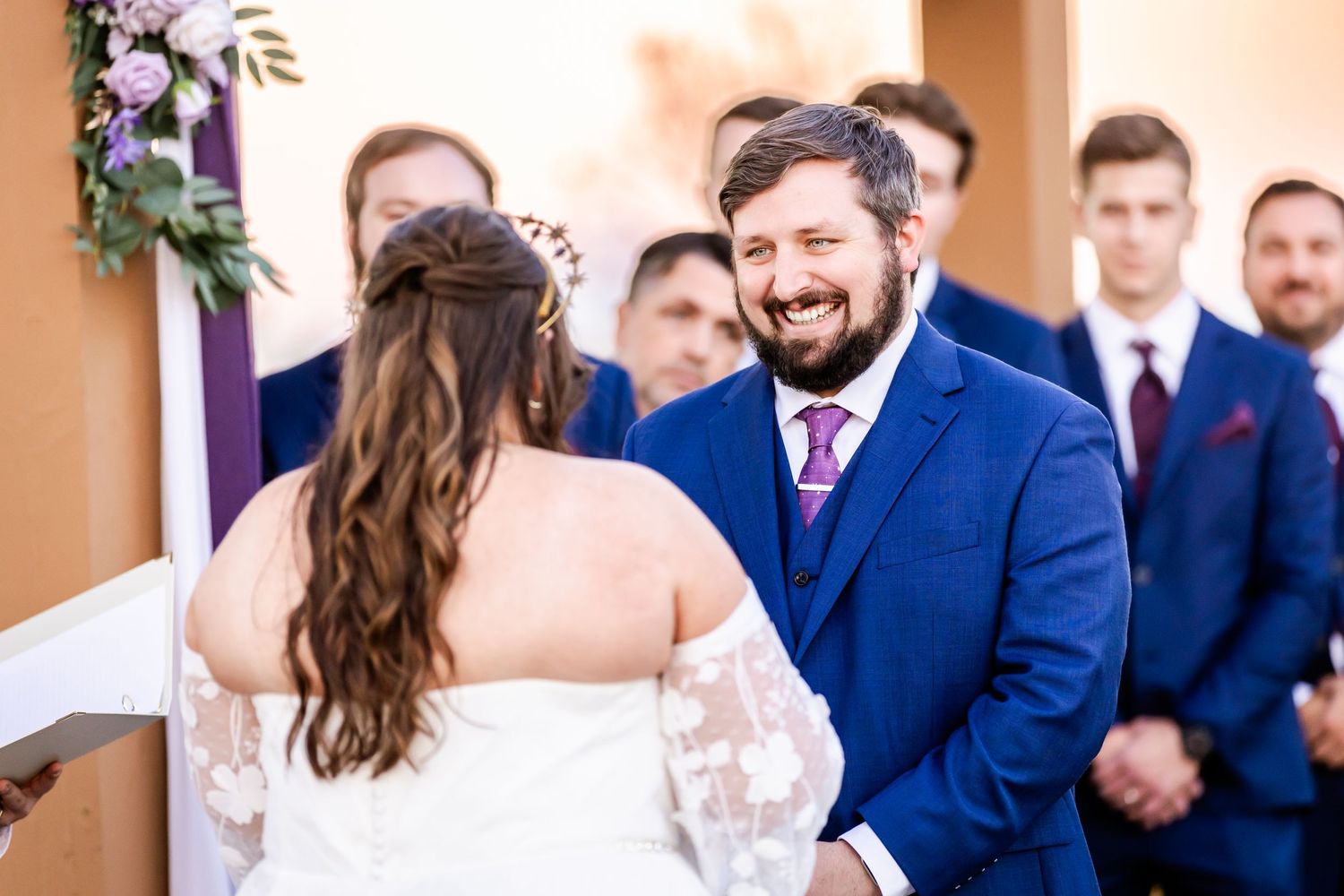 A couple exchanges vows during their wedding ceremony with the wedding party looking on.