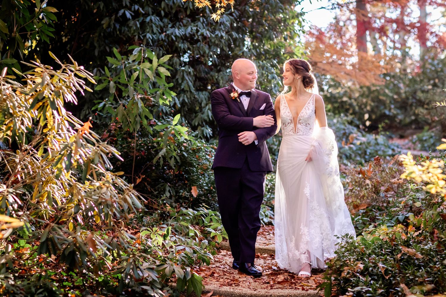 An elegant wedding scene on a garden path surrounded by autumn foliage and golden sunlight.