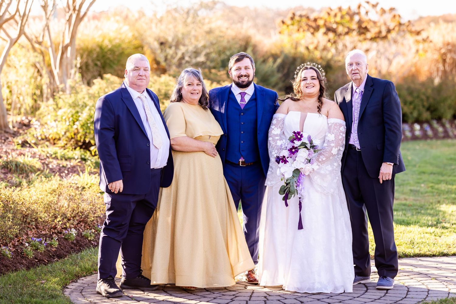 Wedding group photo with couple and family members in formal attire on garden pathway.