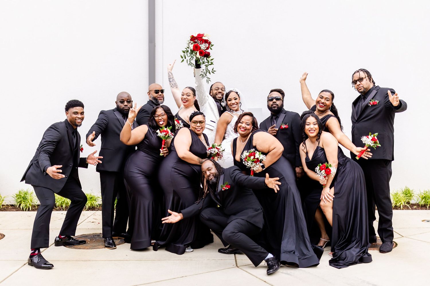 Wedding party strikes fun poses in formal attire against white backdrop.