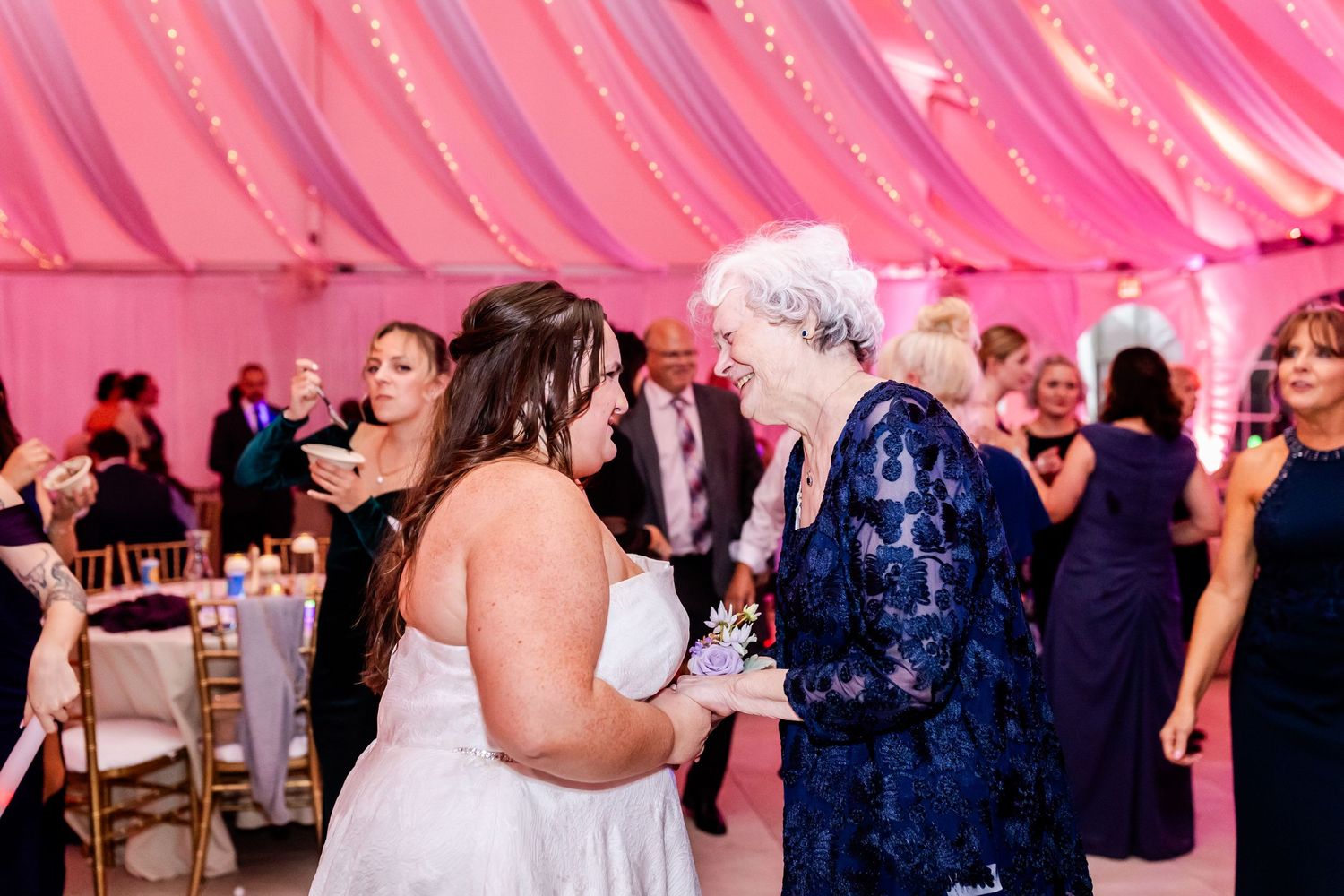 Wedding guests dancing and celebrating under pink-lit draped fabric at an indoor reception.
